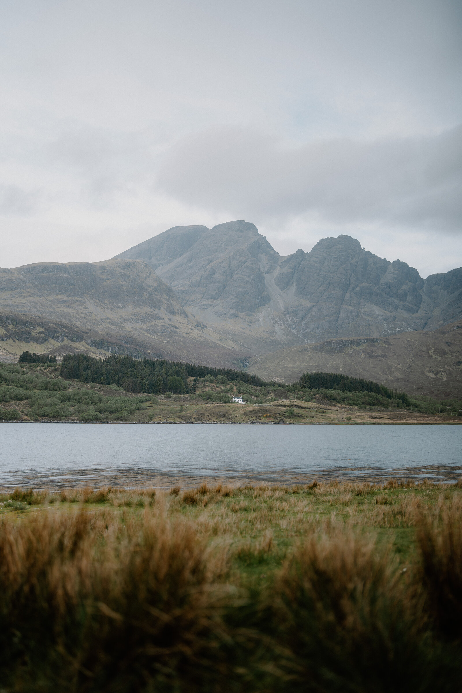 A wire fence lines the moorland above a loch, the misty Cuillin ridge rising beyond.