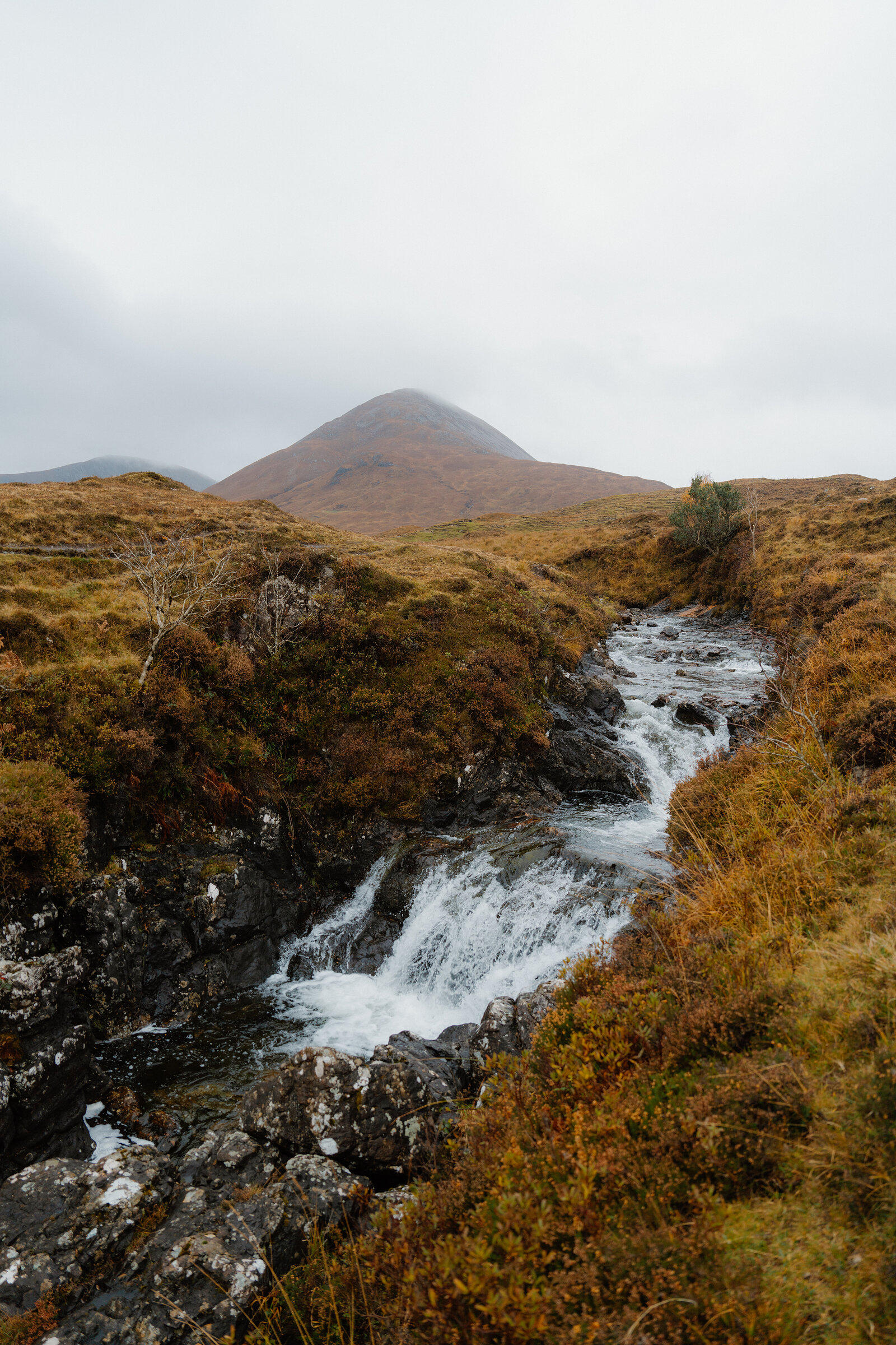 A burn cascades down through peat and dark rock at Torrin, a rounded Red Cuillin hill fading into cloud beyond.