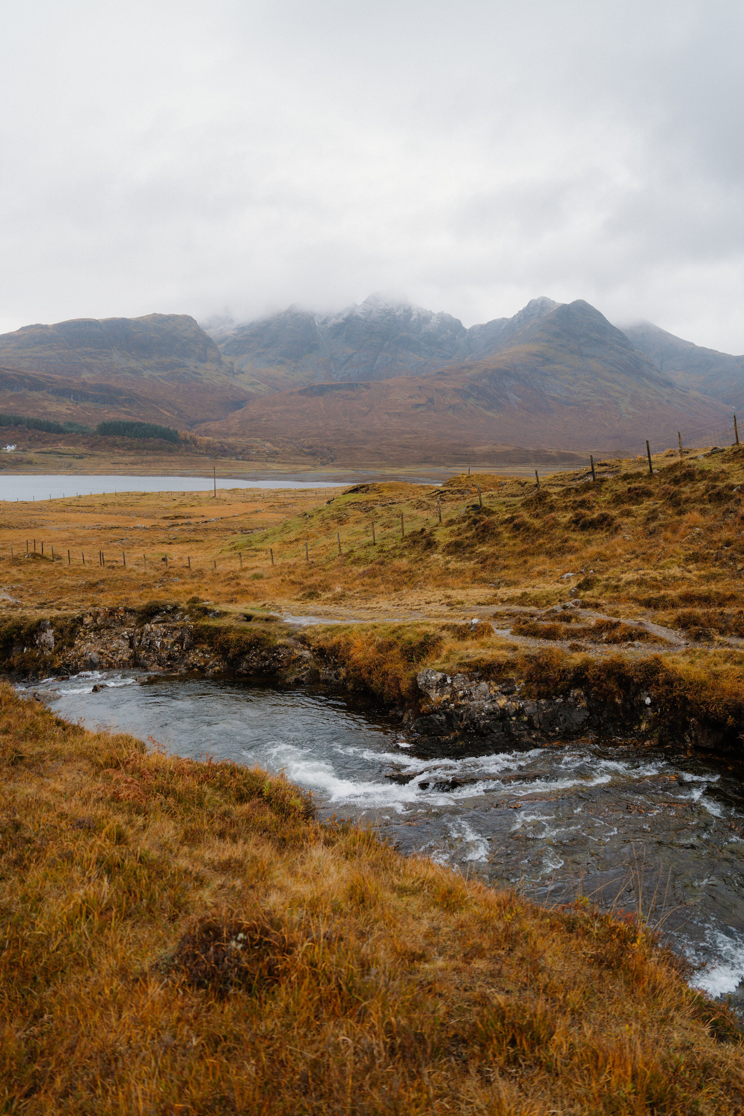 A burn running through autumn moorland towards the loch, Blà Bheinn in cloud behind.