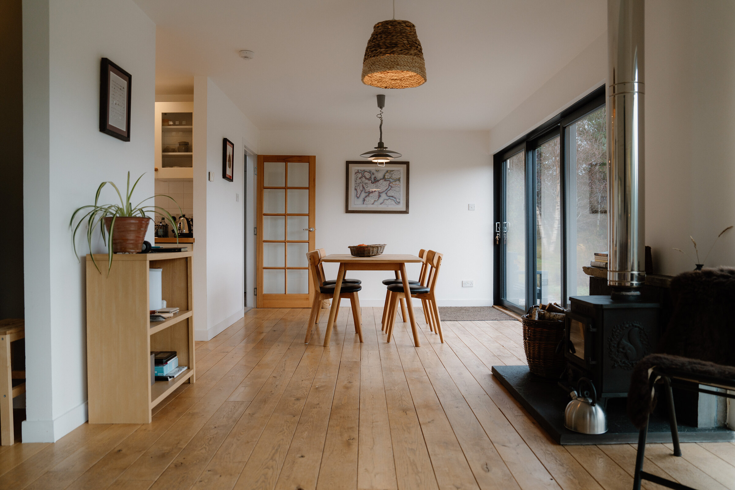 The open-plan room from the kitchen end: the dining table, the wood stove and sliding glass doors onto the croft.