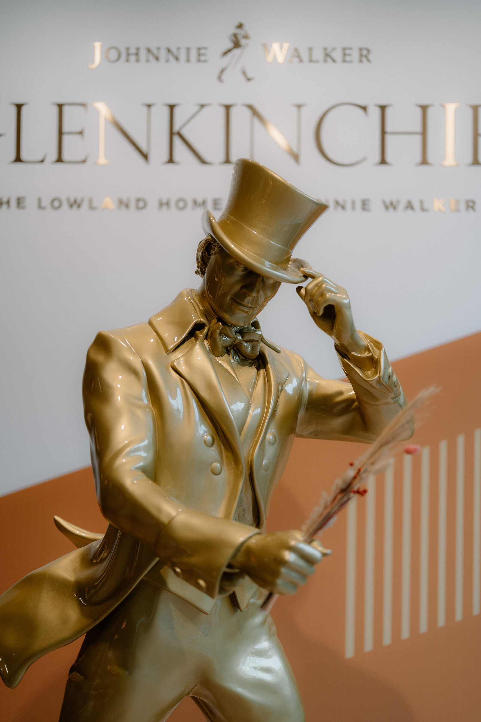A gold statue of the striding Johnnie Walker figure holds sprigs of barley in front of the Glenkinchie branding wall.