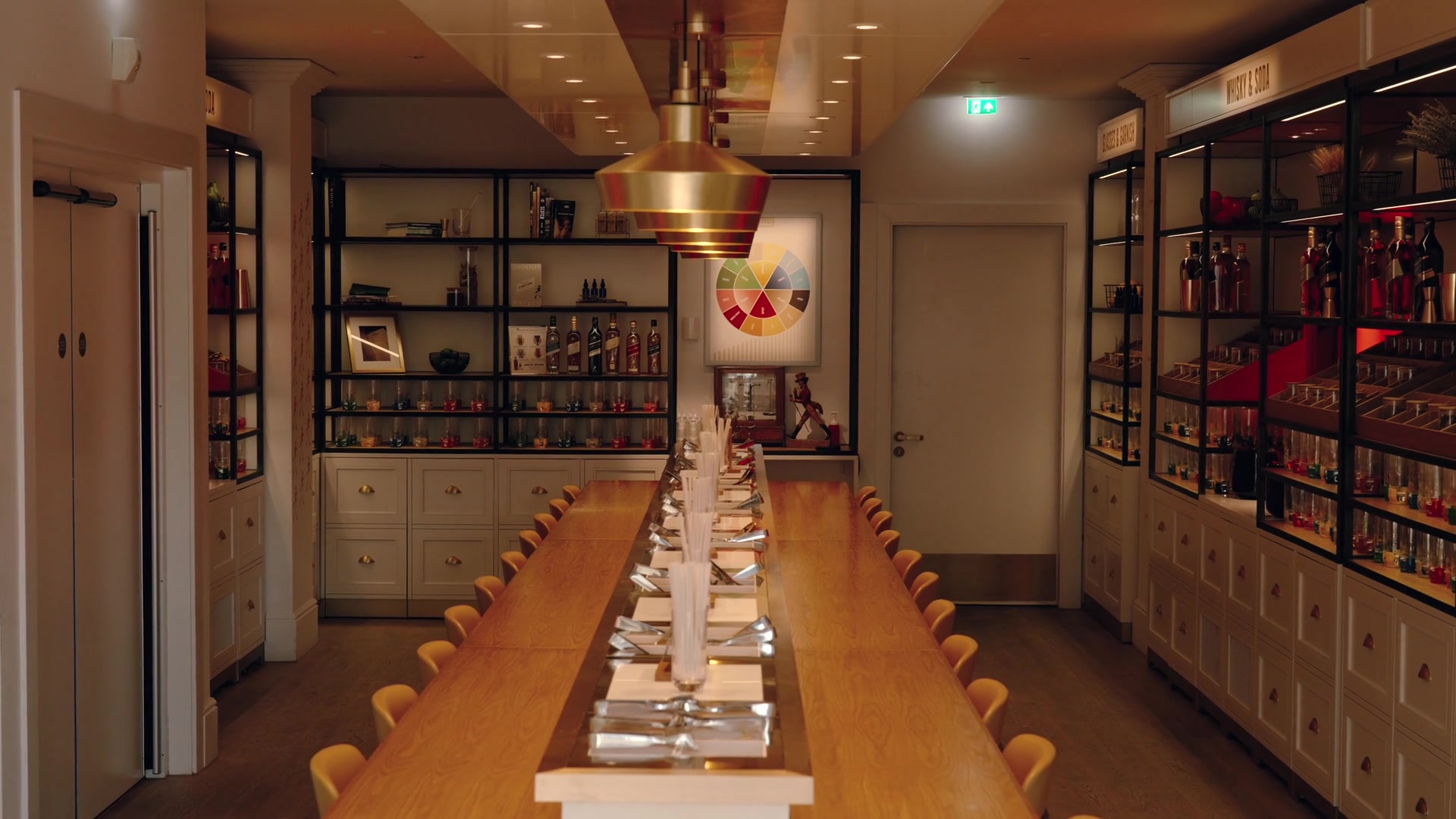 A long table set with straws and glasses runs beneath a brass pendant light, shelves of bottled whisky samples and a flavour wheel chart lining the walls.