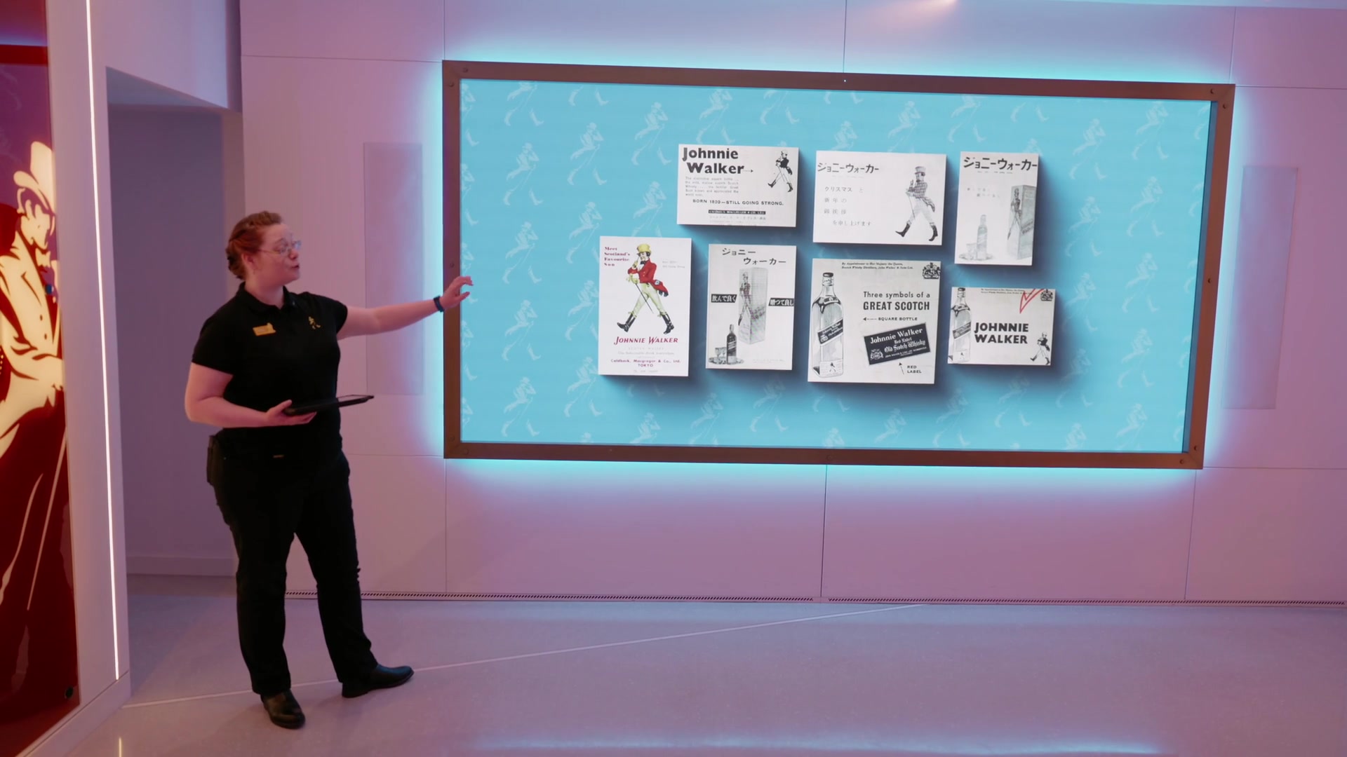 A guide gesturing at a wall of vintage Japanese Johnnie Walker advertisements at the Experience