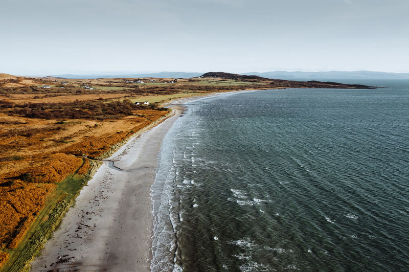 The curve of Corran Sands from the air, waves running onto the beach.