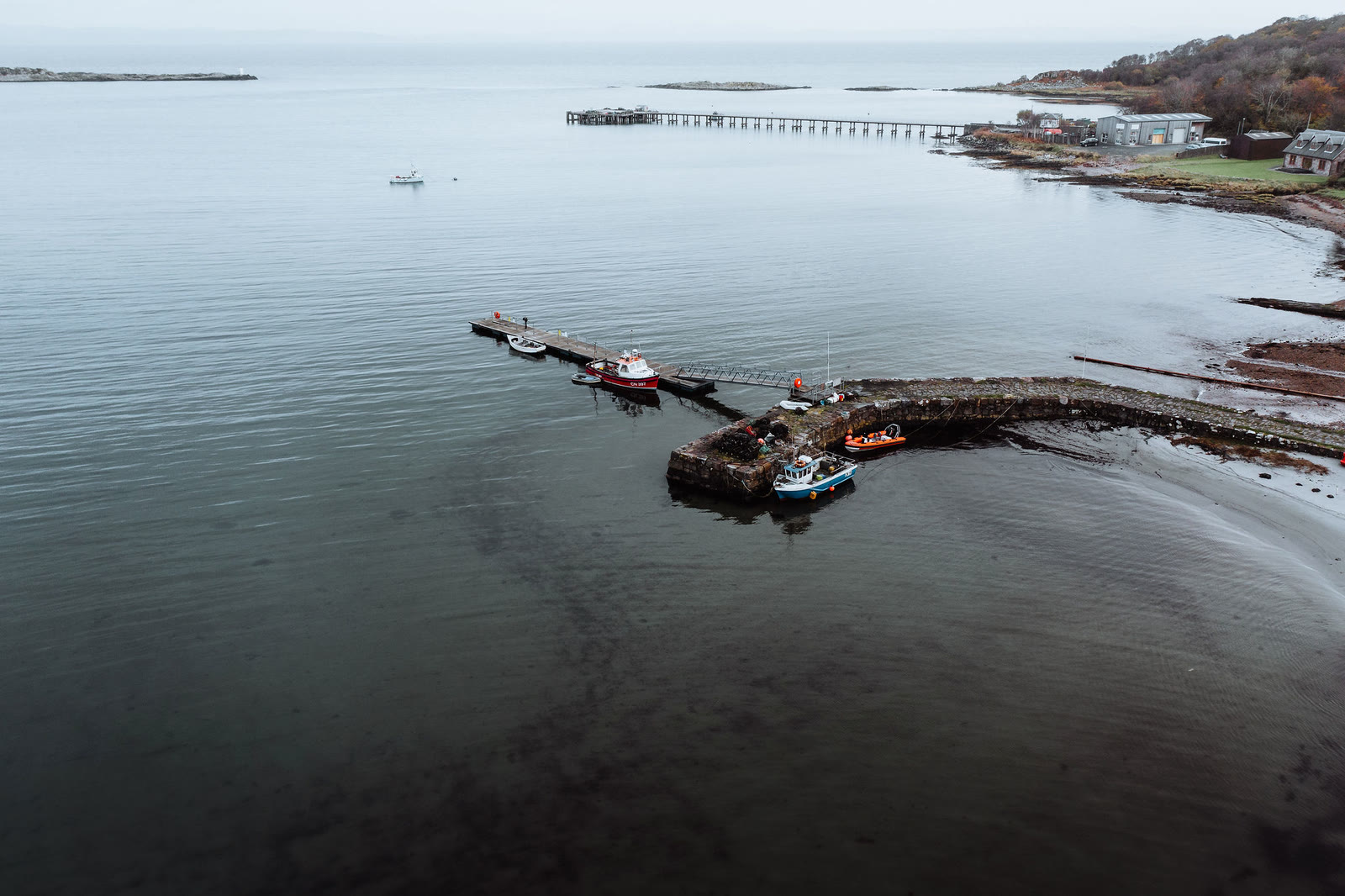 Craighouse pier and its boats from the air, the long pier beyond.