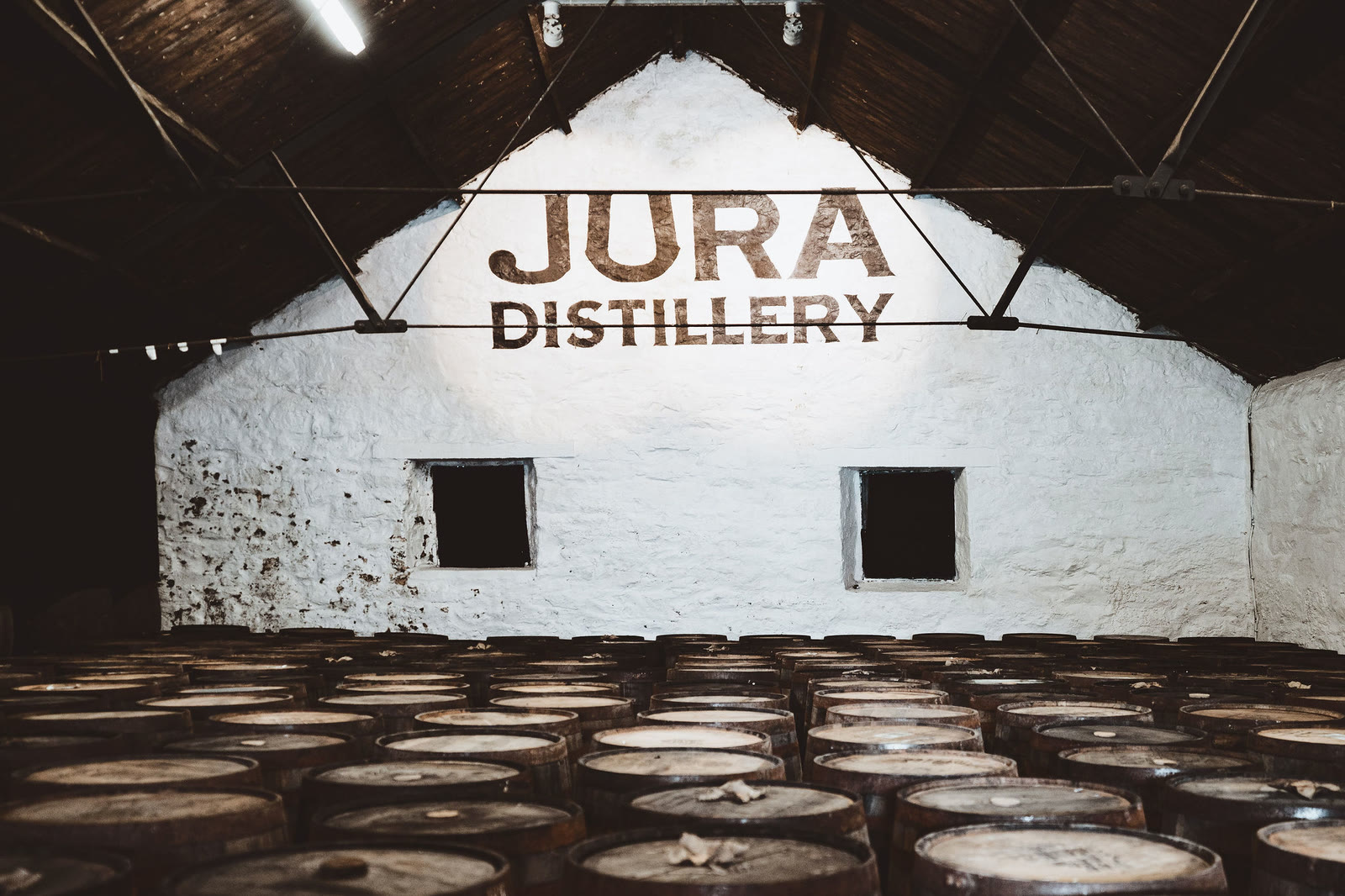 Jura Distillery painted on a whitewashed gable above rows of casks.