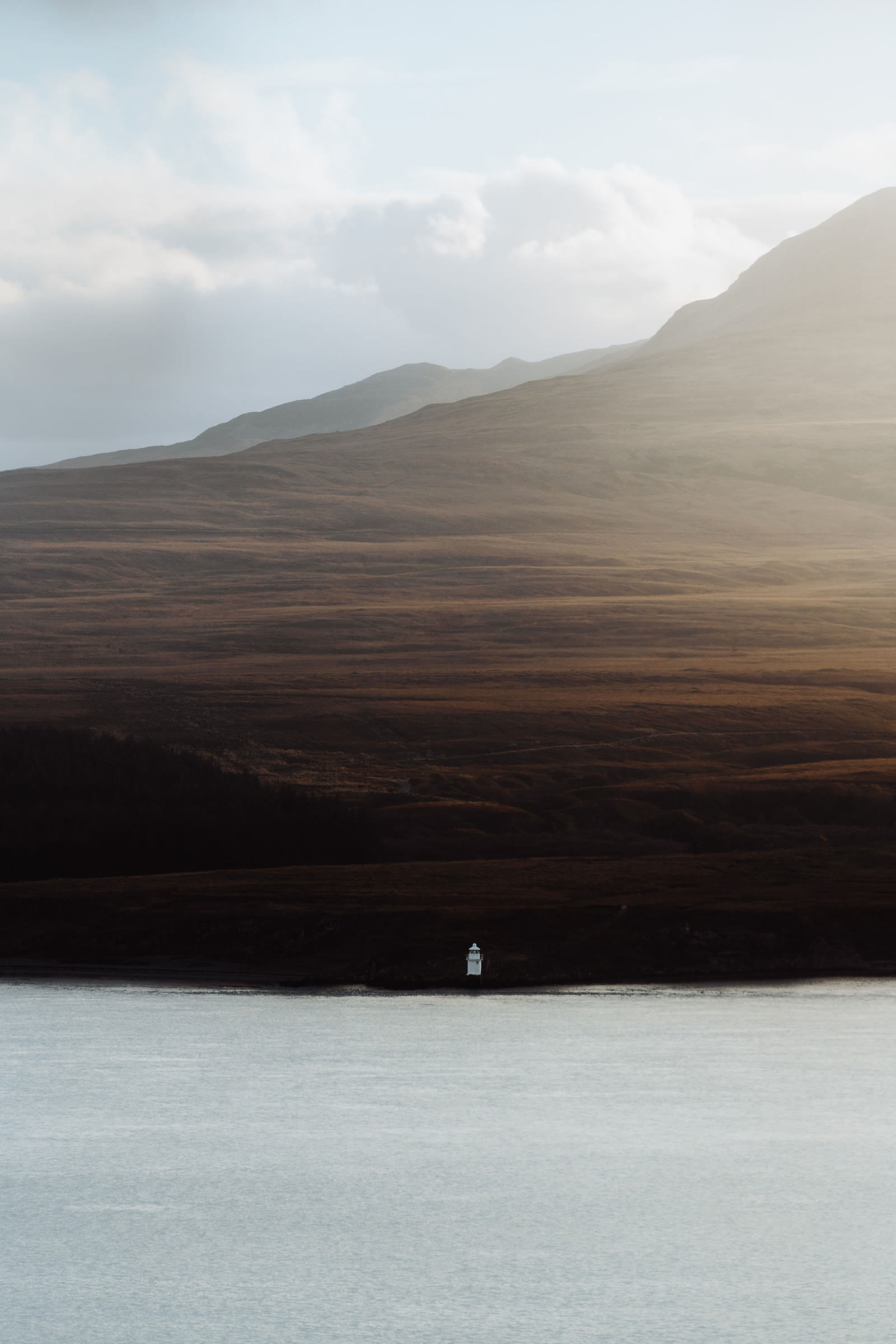 The steep shoulder of one of the Paps of Jura falling to the Sound of Islay, a small white beacon on the shore.