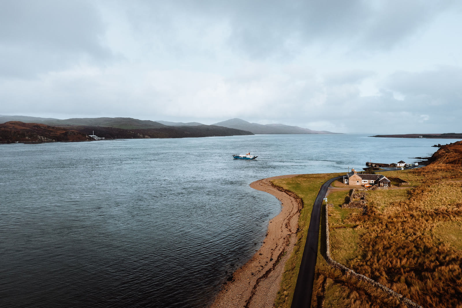 A shore road, a few houses and a small ferry on the Sound of Islay, from the air above Jura.