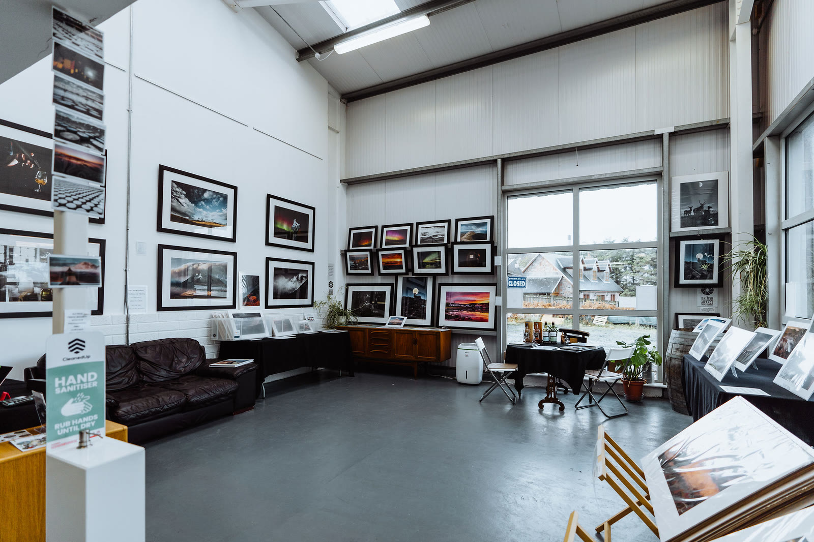 The gallery room with a sofa, framed prints and a window onto the village.