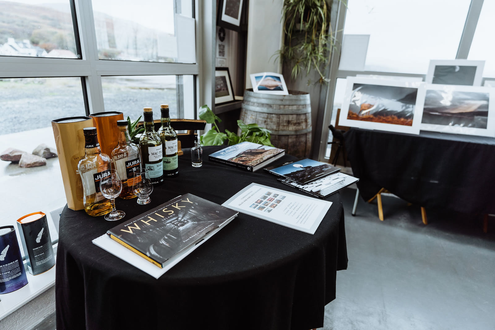 Prints and whisky bottles on a table inside the gallery, a window onto the bay.
