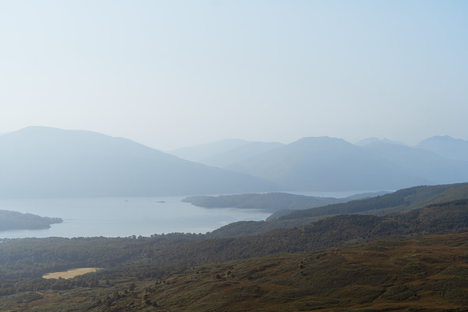 A hazy panoramic view over a loch dotted with wooded islands, hills fading into the distance on either side.