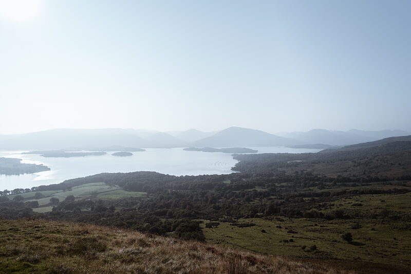 A hazy panoramic view over a loch dotted with wooded islands, hills fading into the distance on either side.