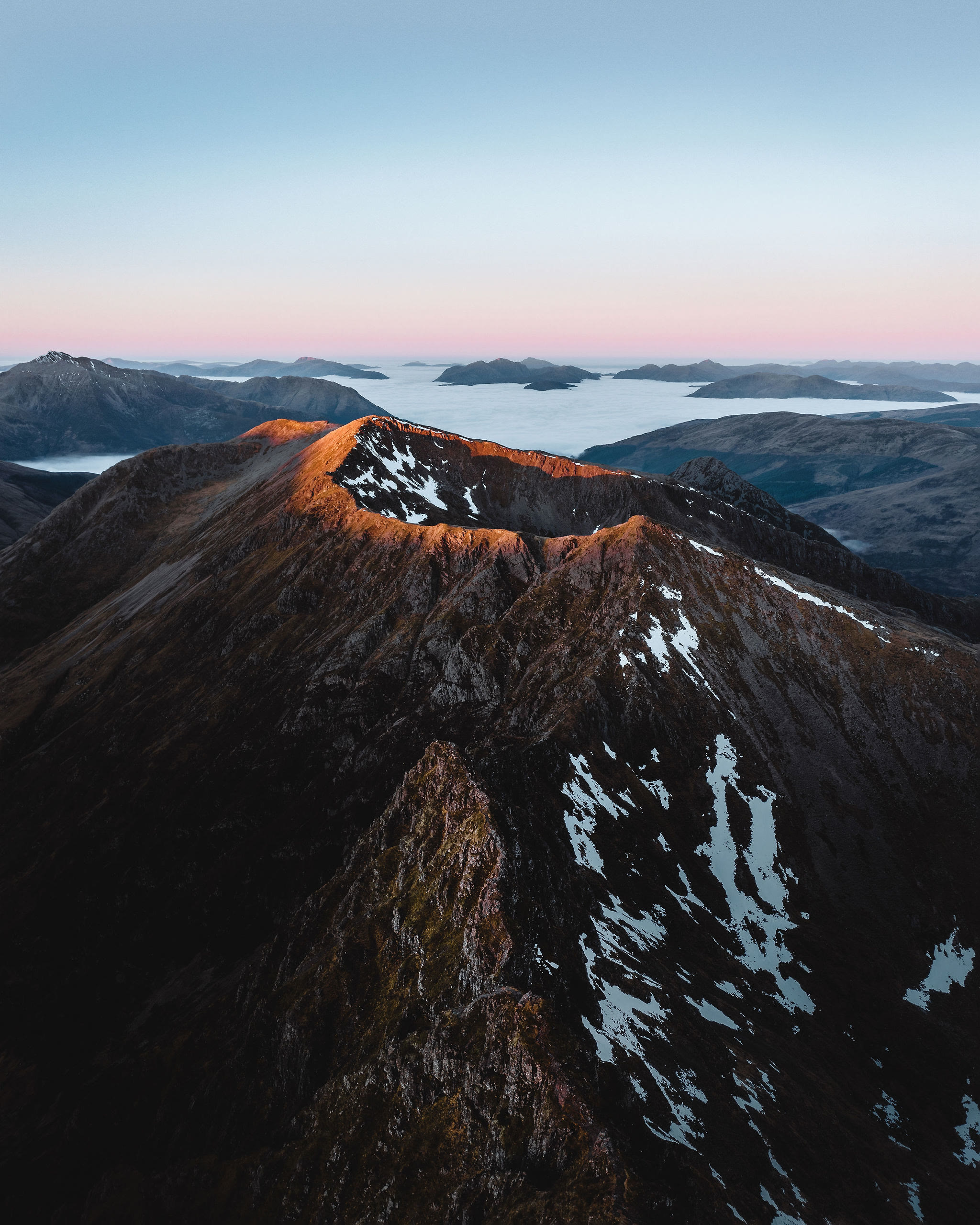 The Aonach Eagach from above at dawn, steep snow-streaked rock in the foreground.
