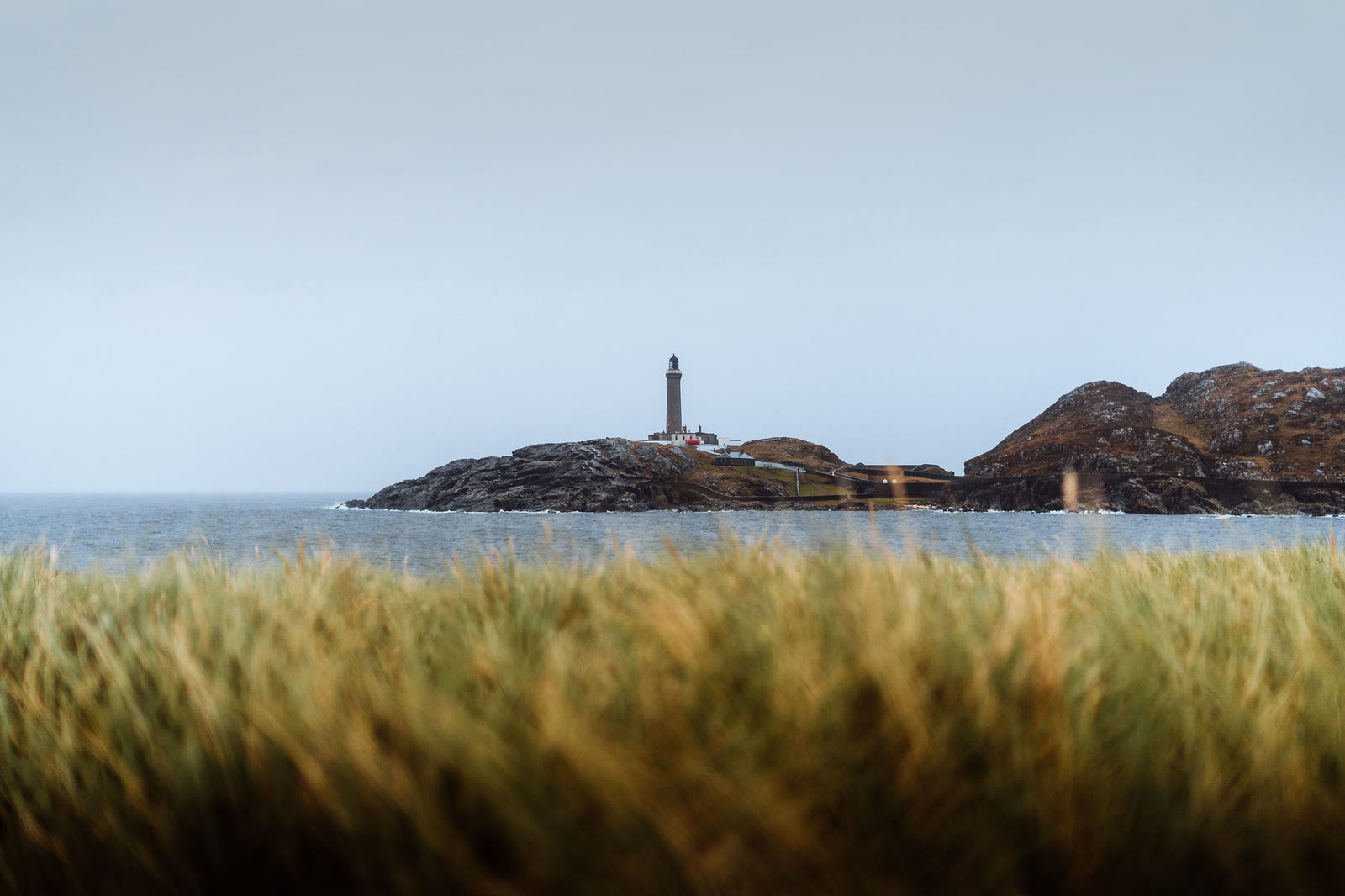Ardnamurchan Lighthouse on its headland seen across the water over marram grass.