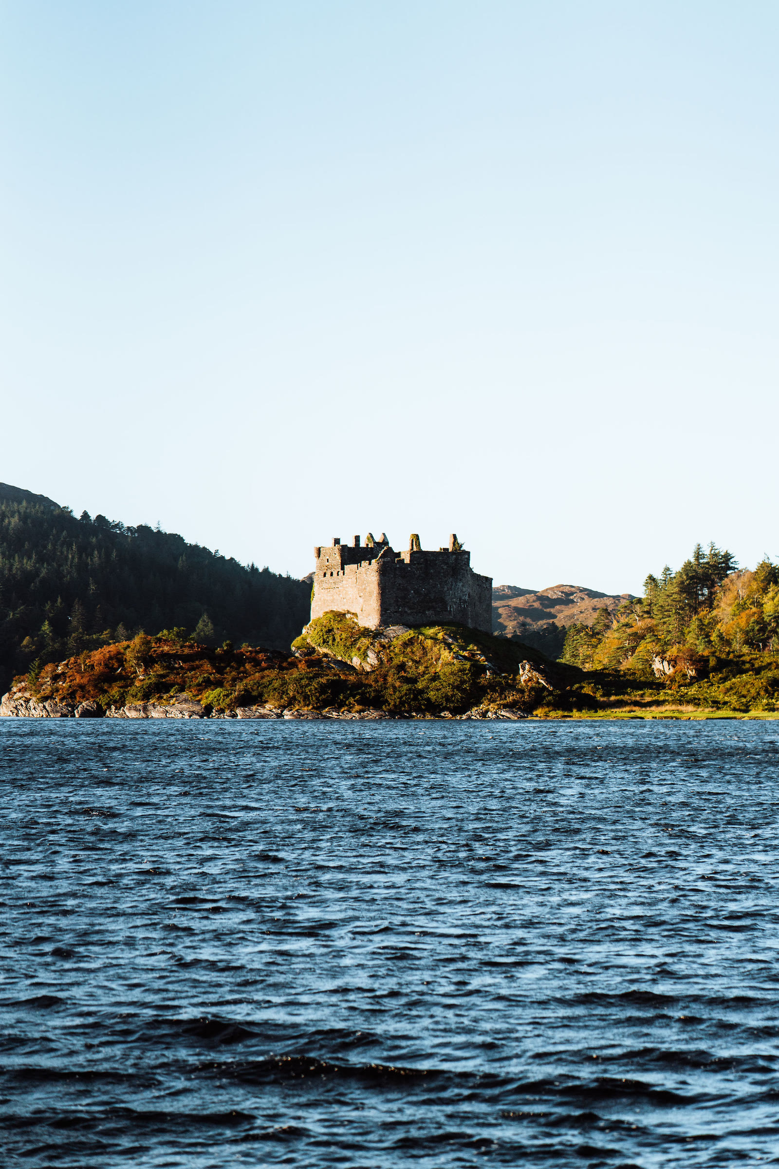 Castle Tioram across the water of Loch Moidart, its walls catching the sun.
