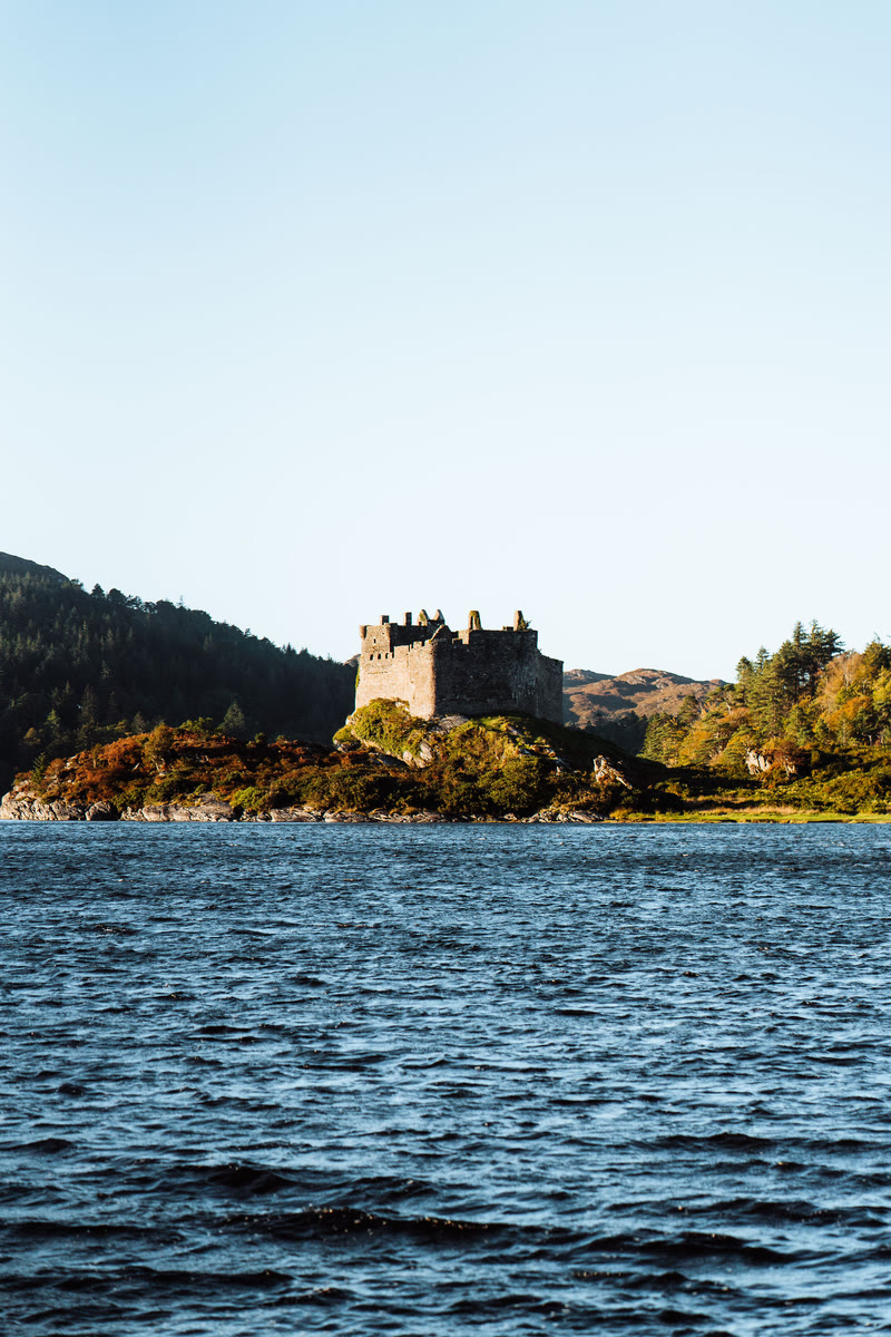 Castle Tioram across the water of Loch Moidart, its walls catching the sun.