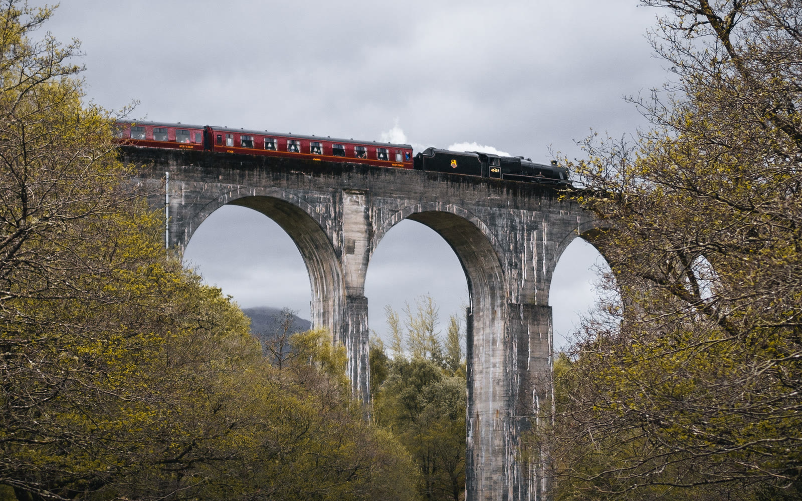 The Jacobite steam train crossing the tall arches of the Glenfinnan Viaduct, seen from below.