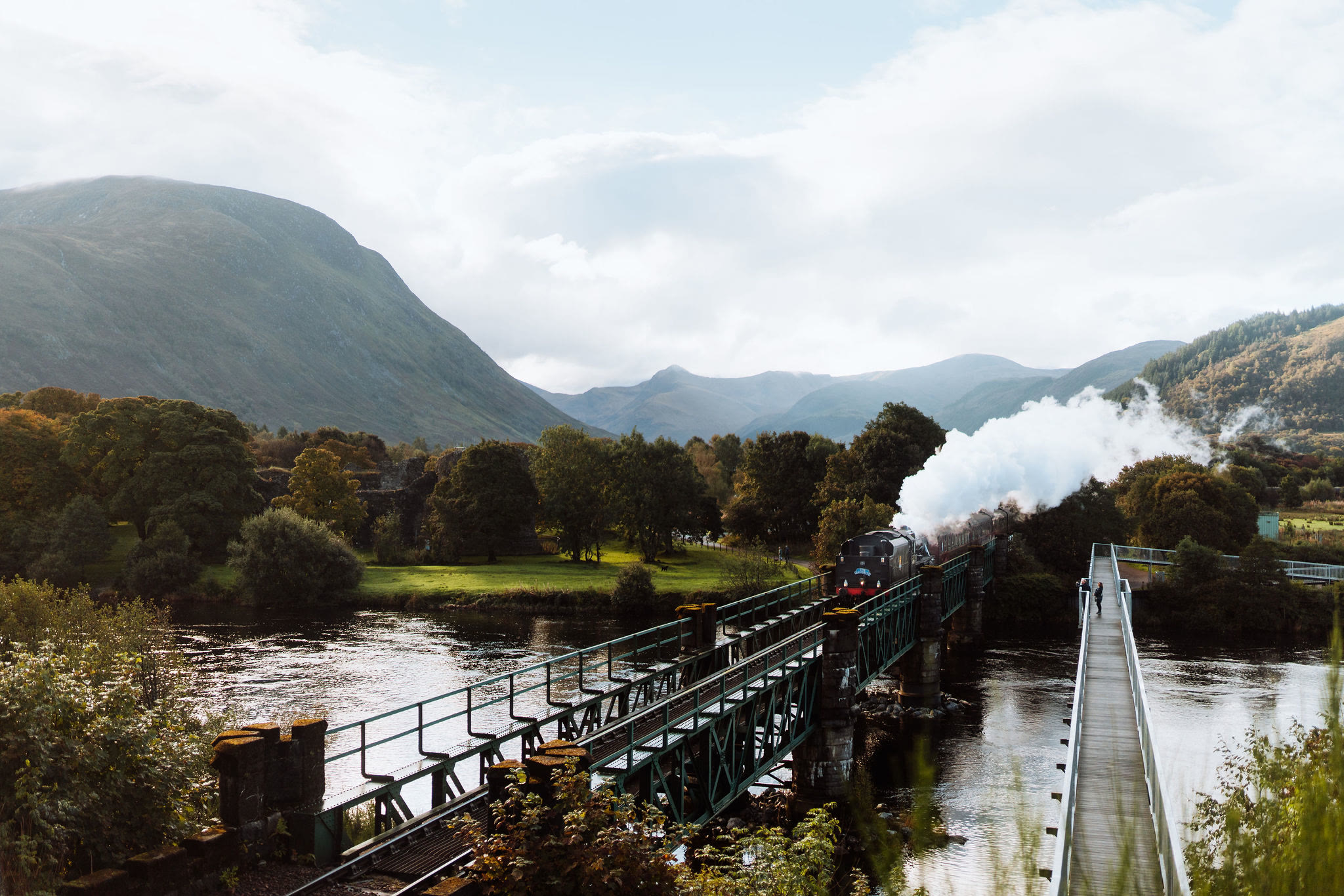 The Jacobite steam train on the bridge over the River Lochy, a footbridge running beside it.