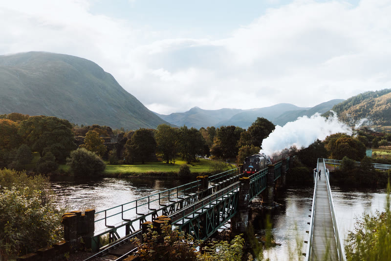 The Jacobite steam train on the bridge over the River Lochy, a footbridge running beside it.