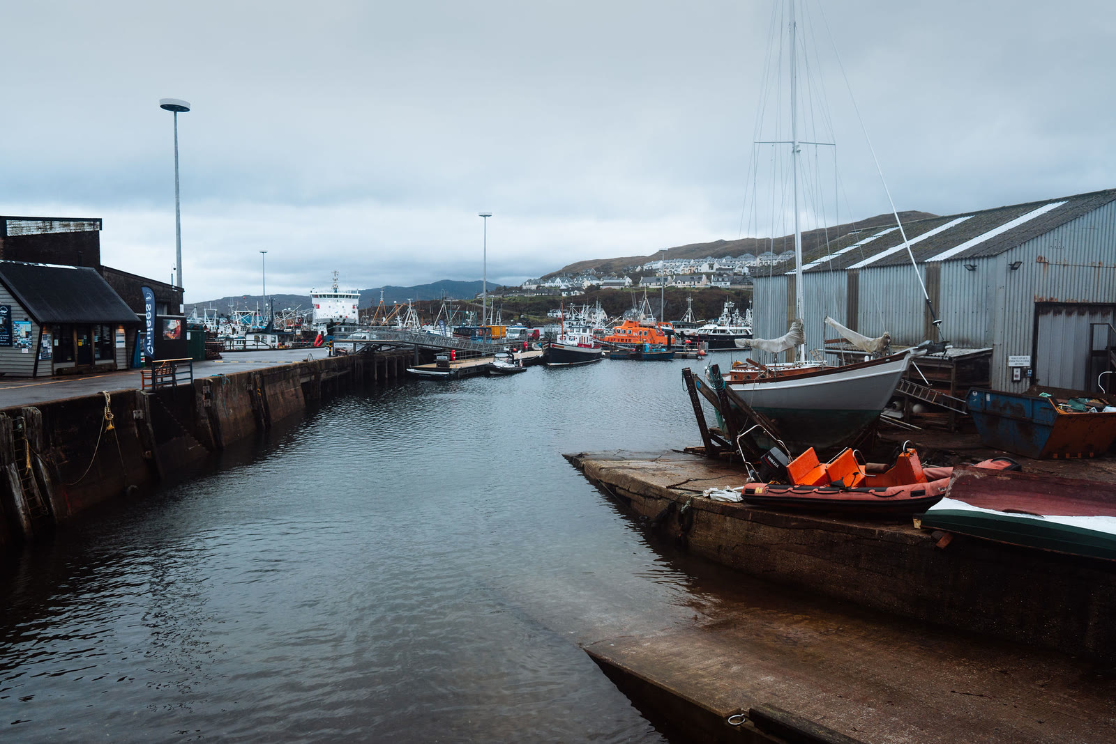 Mallaig harbour, fishing boats along the quay under grey cloud.