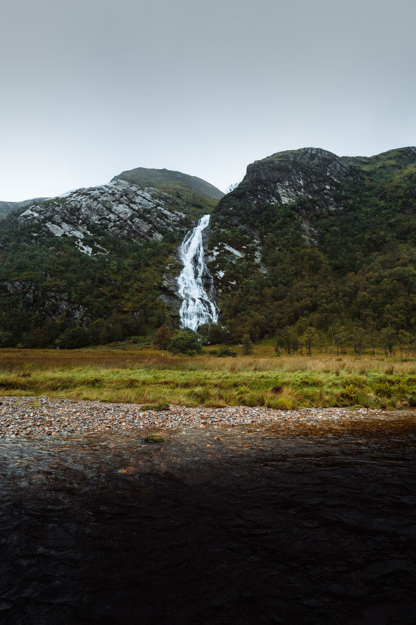 Steall Falls dropping down its rock face above the river shingle in Glen Nevis.