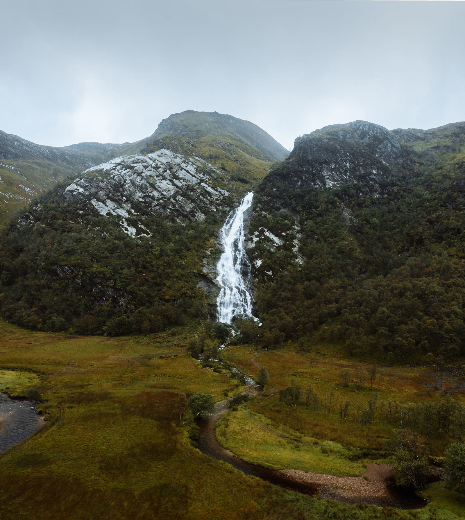 Steall Falls from the air, a white ribbon of water dropping between two rocky hills to the river winding across the flat floor of upper Glen Nevis.