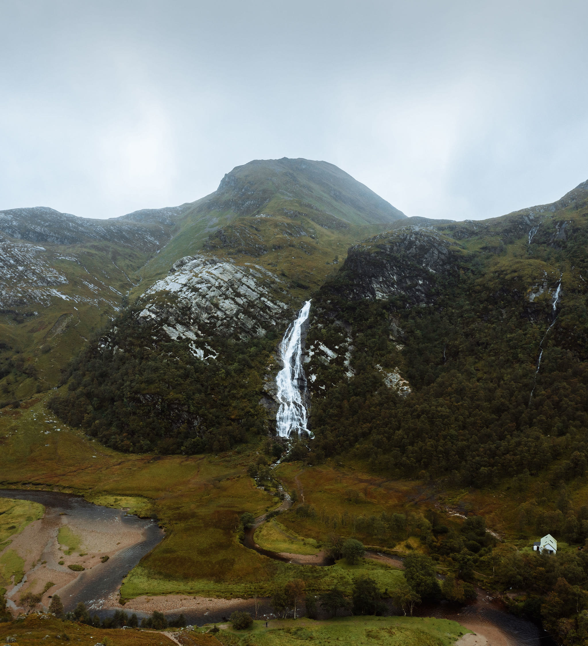 Steall Falls from the air, with An Gearanach above them and the river bend in the meadow below.