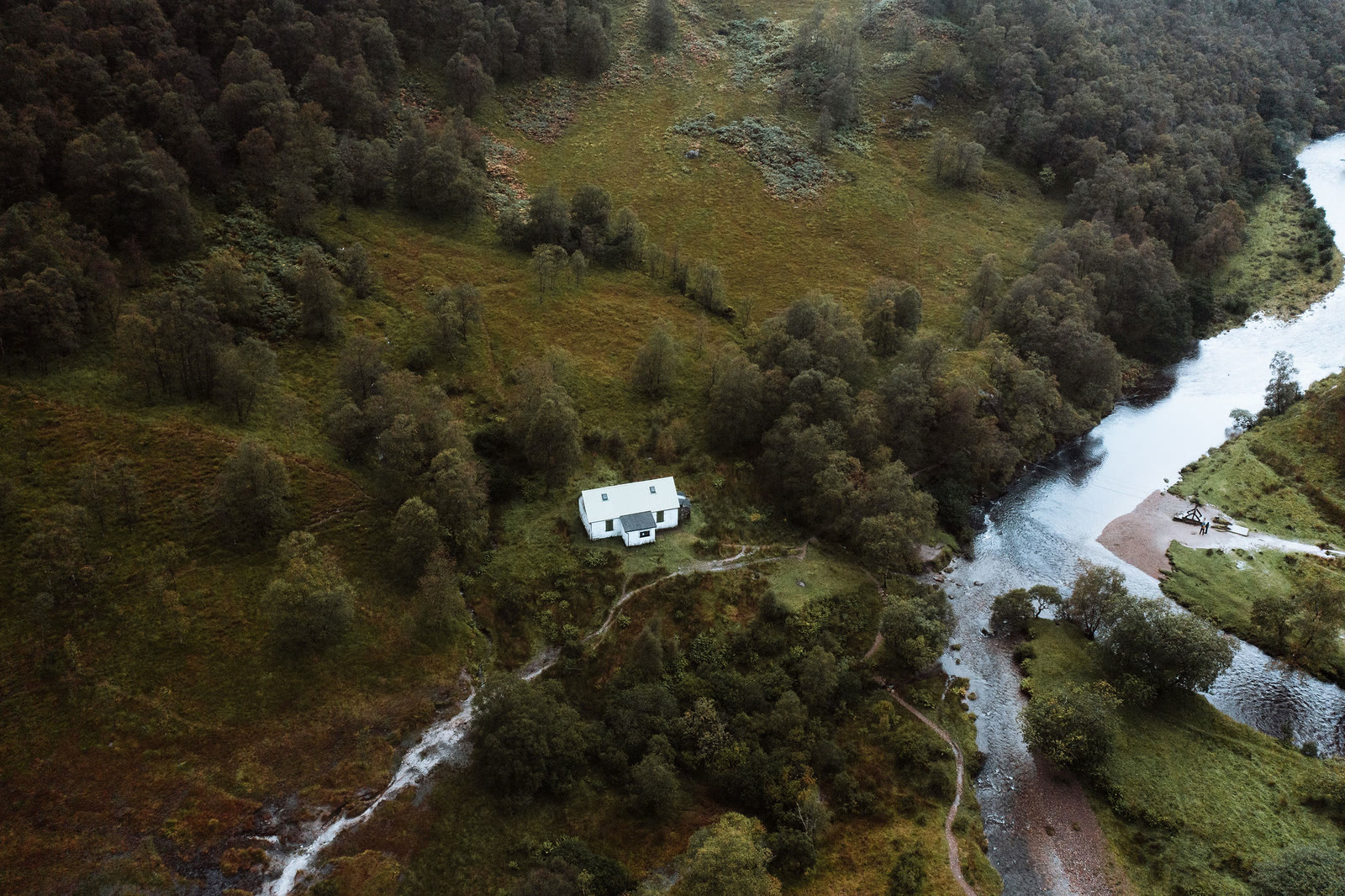 The white Steall hut among birch trees by the river in upper Glen Nevis, seen from the air.