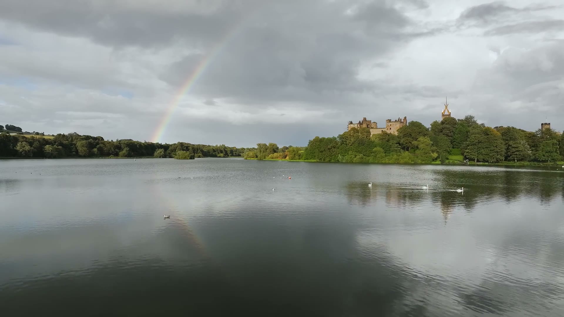 A rainbow over Linlithgow Palace and its loch between showers, swans on the water.