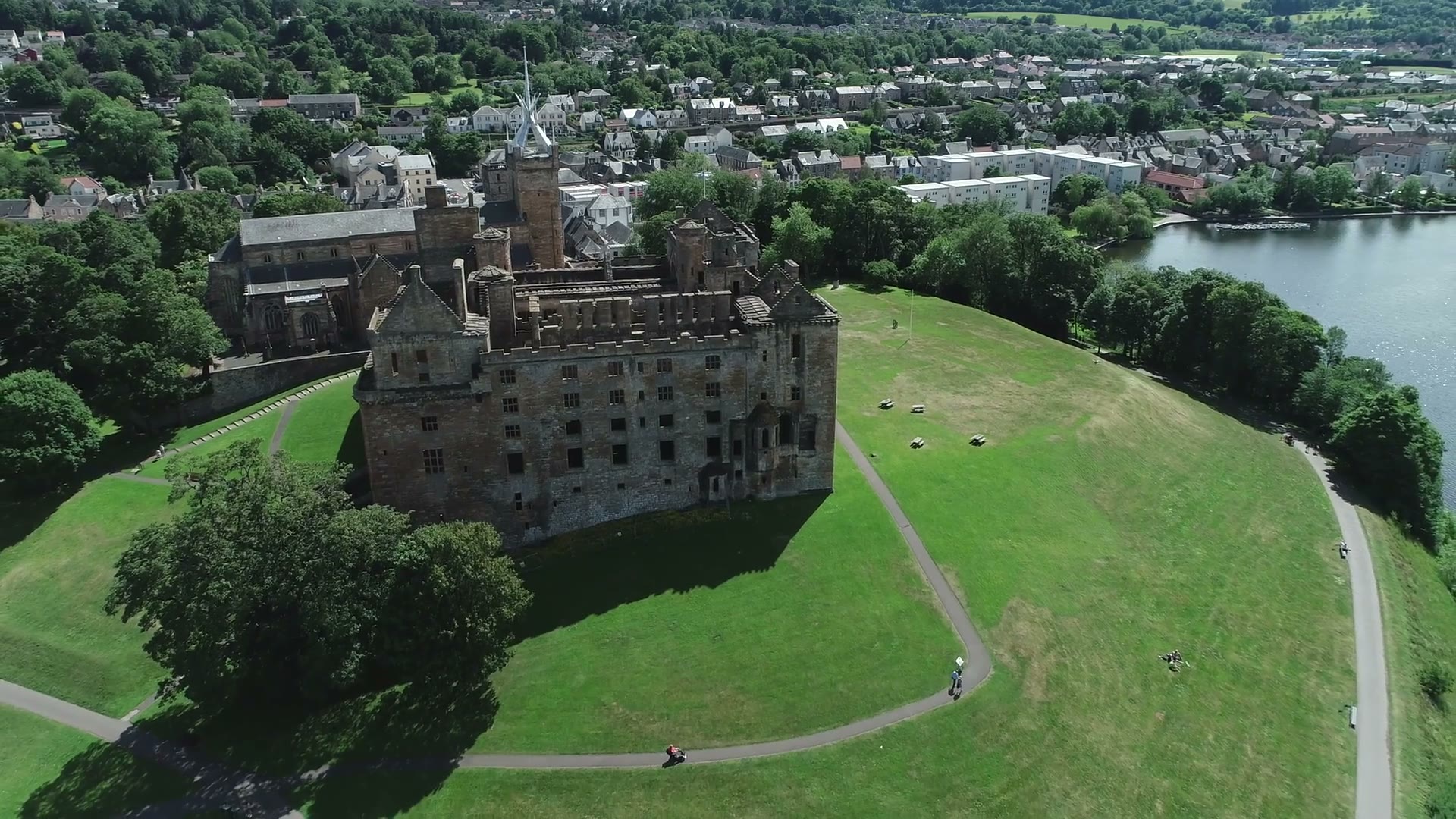Linlithgow Palace from the air on the green Peel, paths curving round it, the loch at its side and the town behind.
