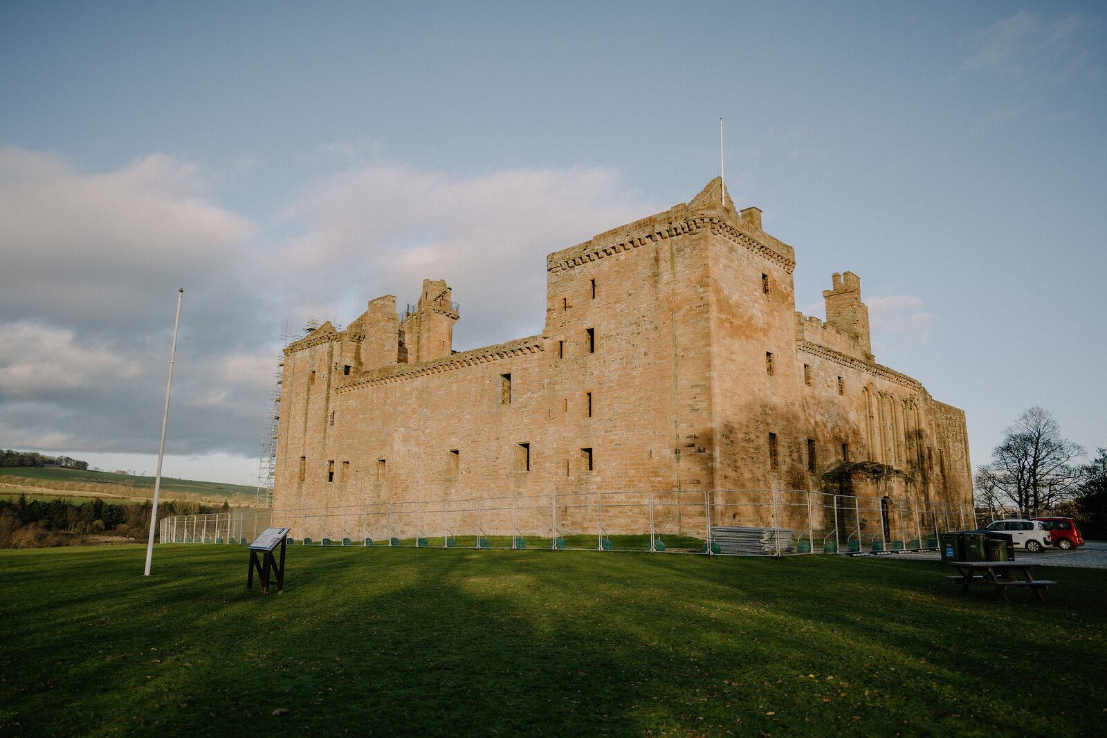A castellated sandstone palace with corner towers and crow-stepped gables stands on a grass lawn, a cannon and flagpole in the foreground.