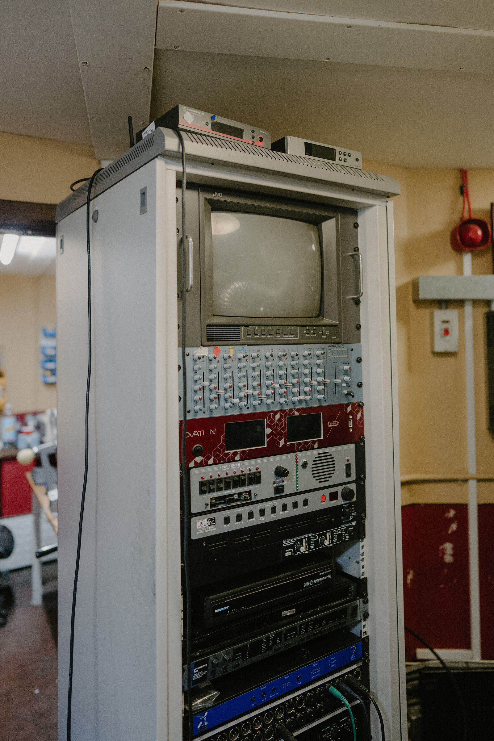 A vintage equipment rack holds a small monitor screen, mixing desk and audio units in a cinema projection room.