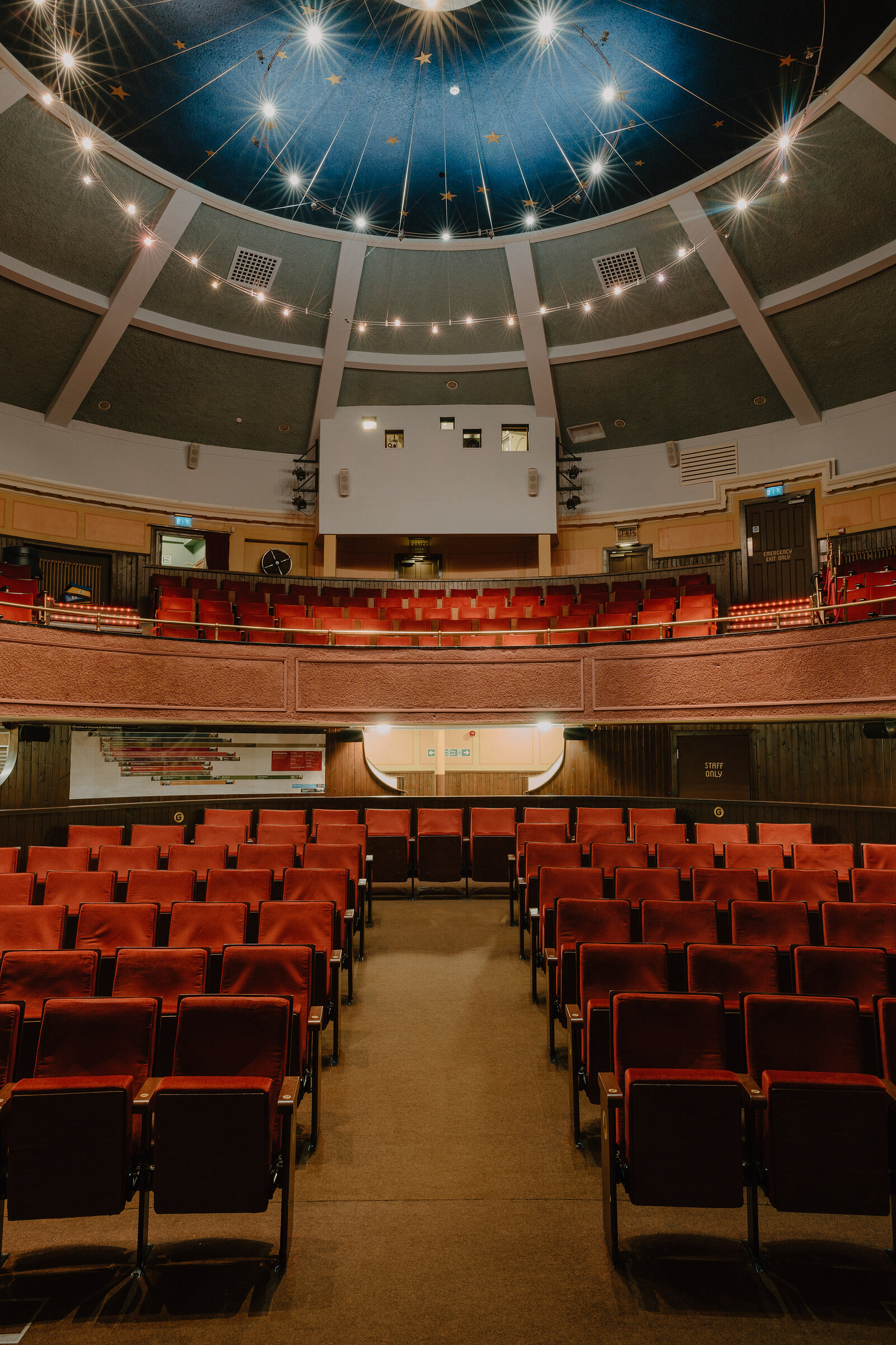 A star-painted domed ceiling strung with lights arcs above a curved balcony of red seats overlooking a lower tier of red theatre seating.