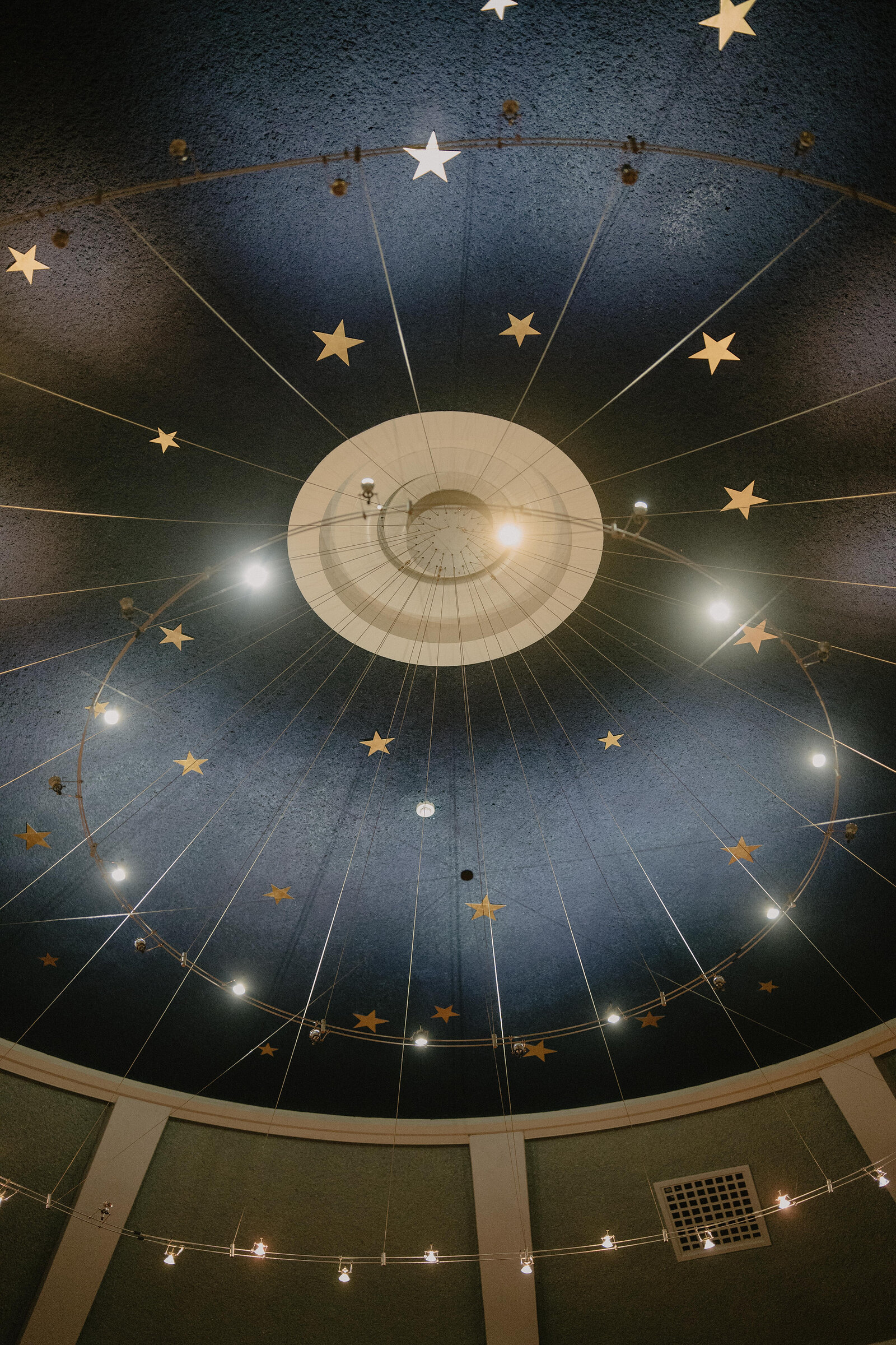 A domed theatre ceiling painted with gold stars radiates from a central lantern hung with lights, string lights looping around the dome above a balcony rail.