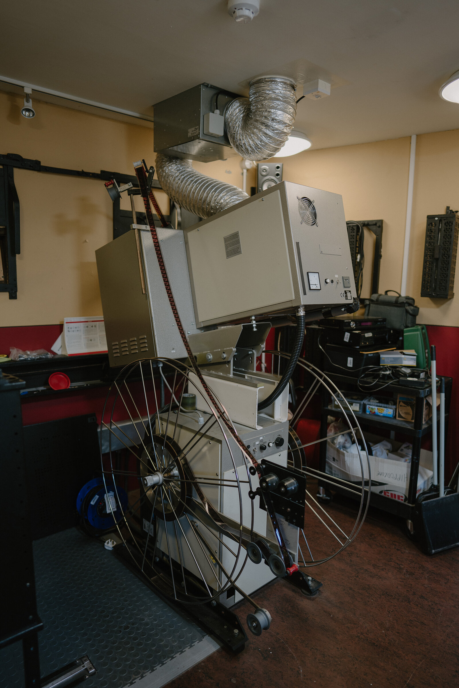 A projection room holds a large film projector with its reels and sprockets, ducting running from its housing to the ceiling.