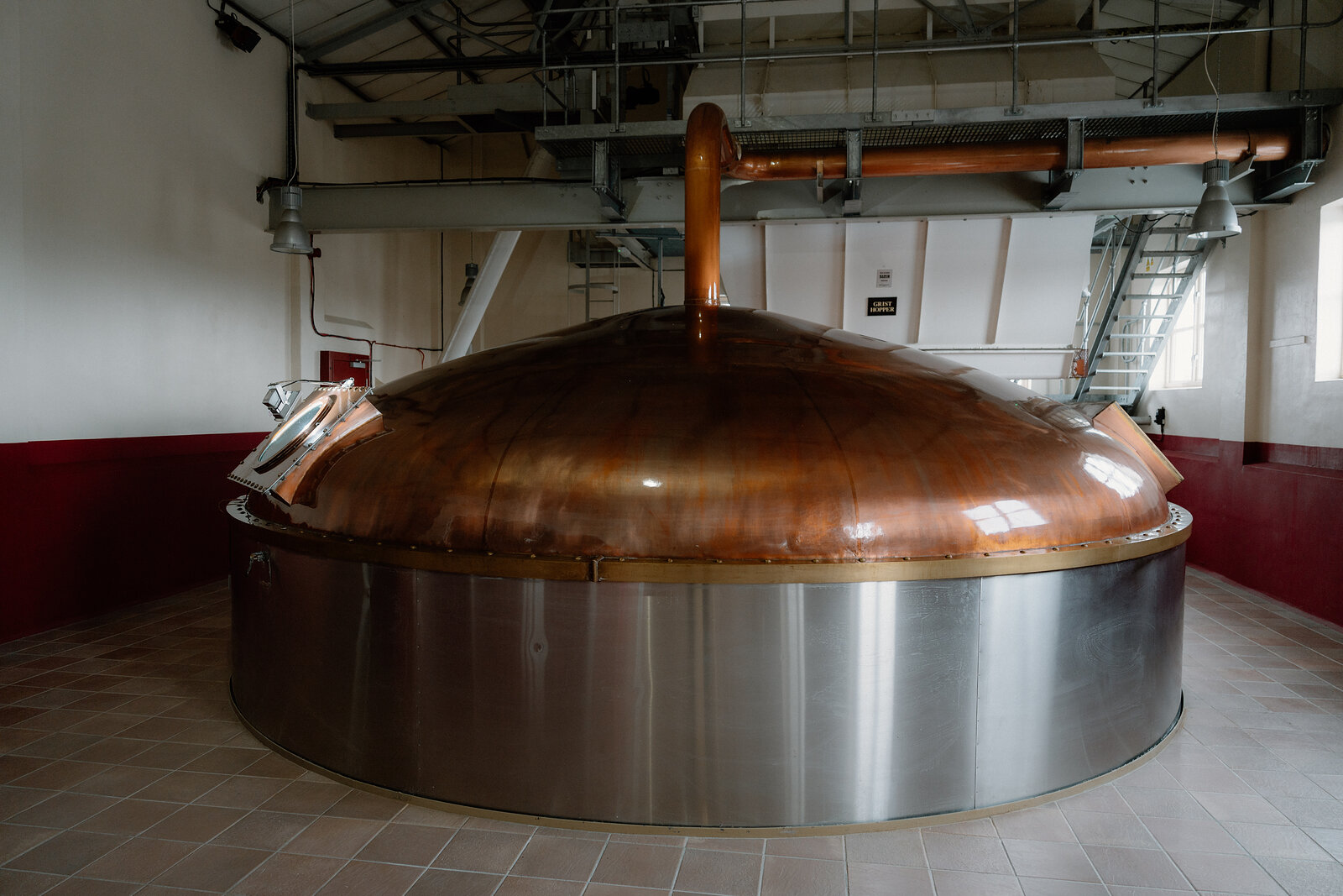 A large copper mash tun with a domed lid stands on a tiled floor in Cardhu's distillery hall.