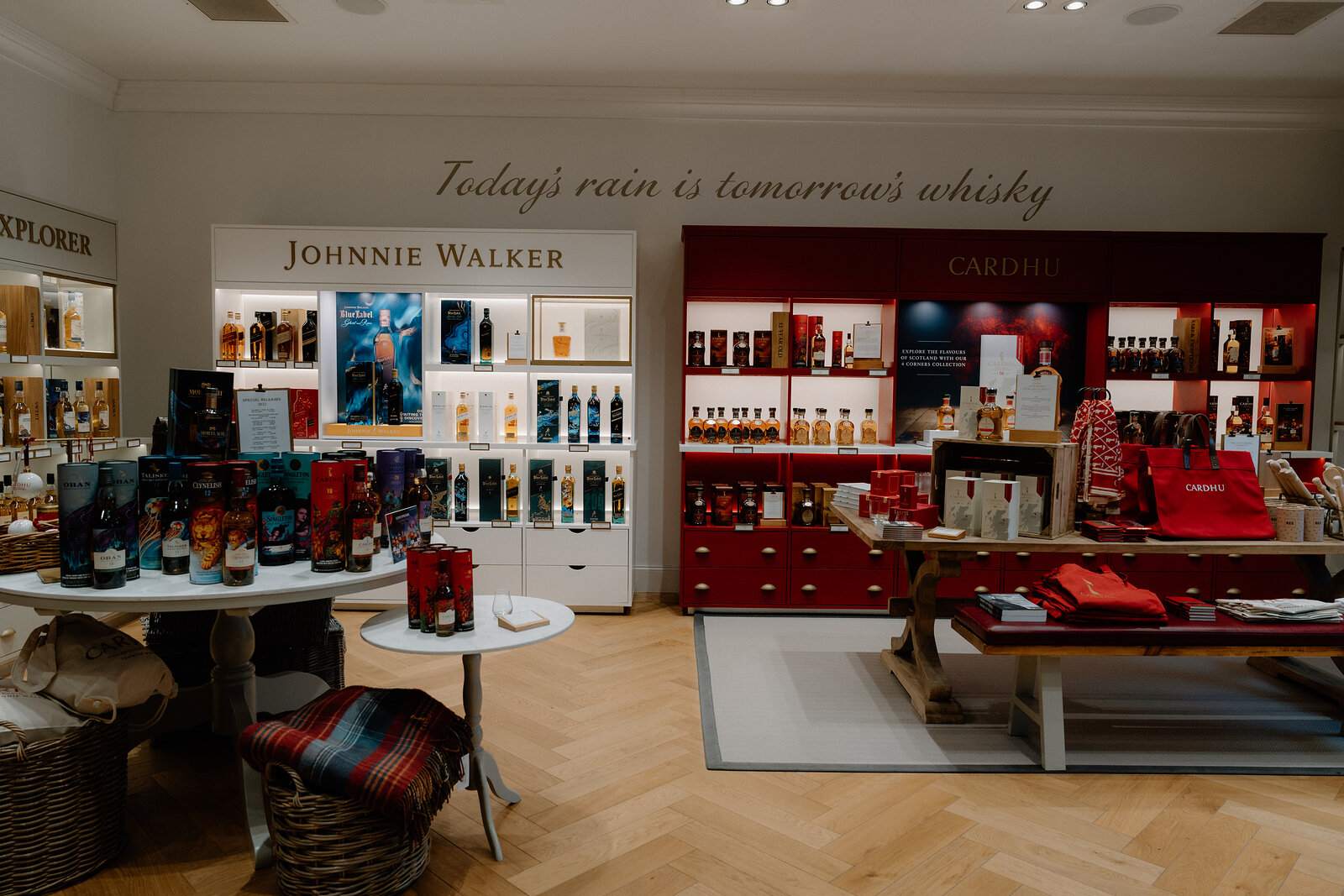 A wall reading 'Today's rain is tomorrow's whisky' overlooks Johnnie Walker and Cardhu merchandise in the distillery gift shop.