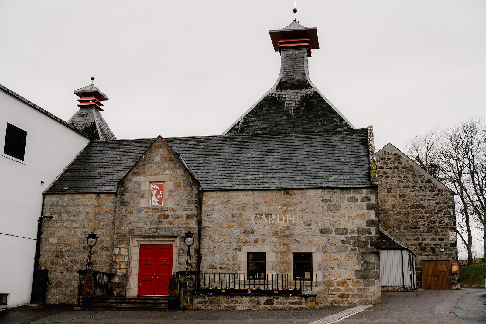 Cardhu's stone distillery building has pagoda-roofed vents and a red door beside its lettered facade.