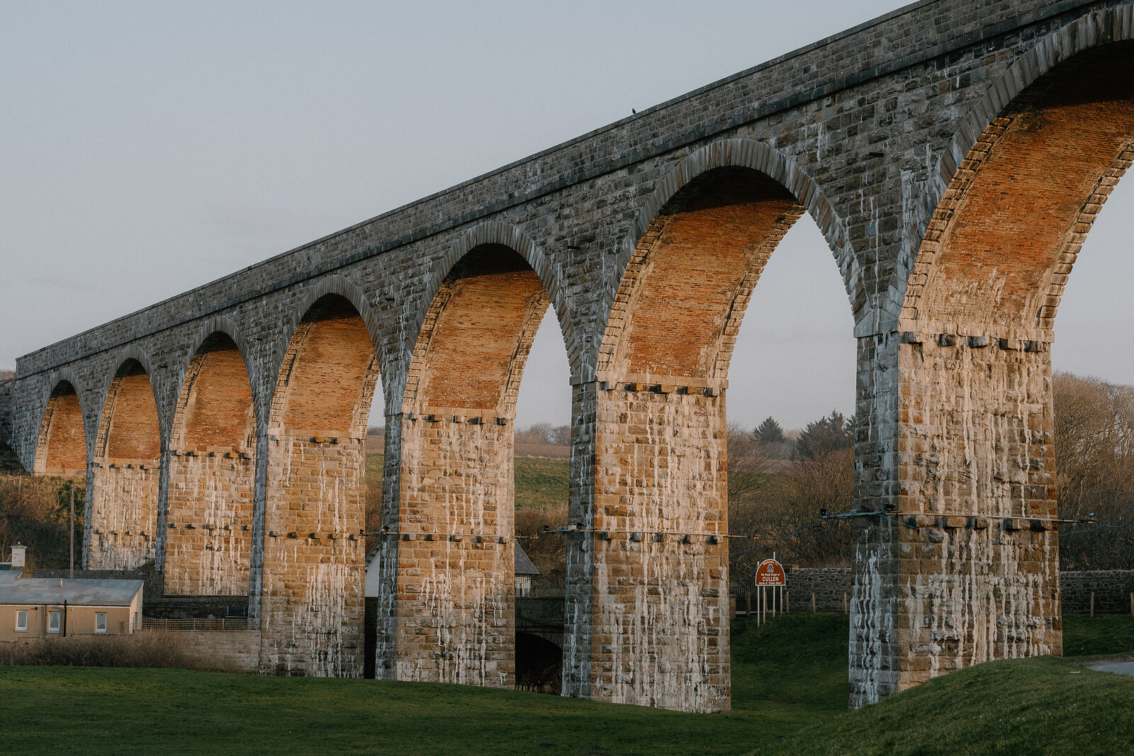 A multi-arched brick and stone railway viaduct spans a grassy valley in Moray.