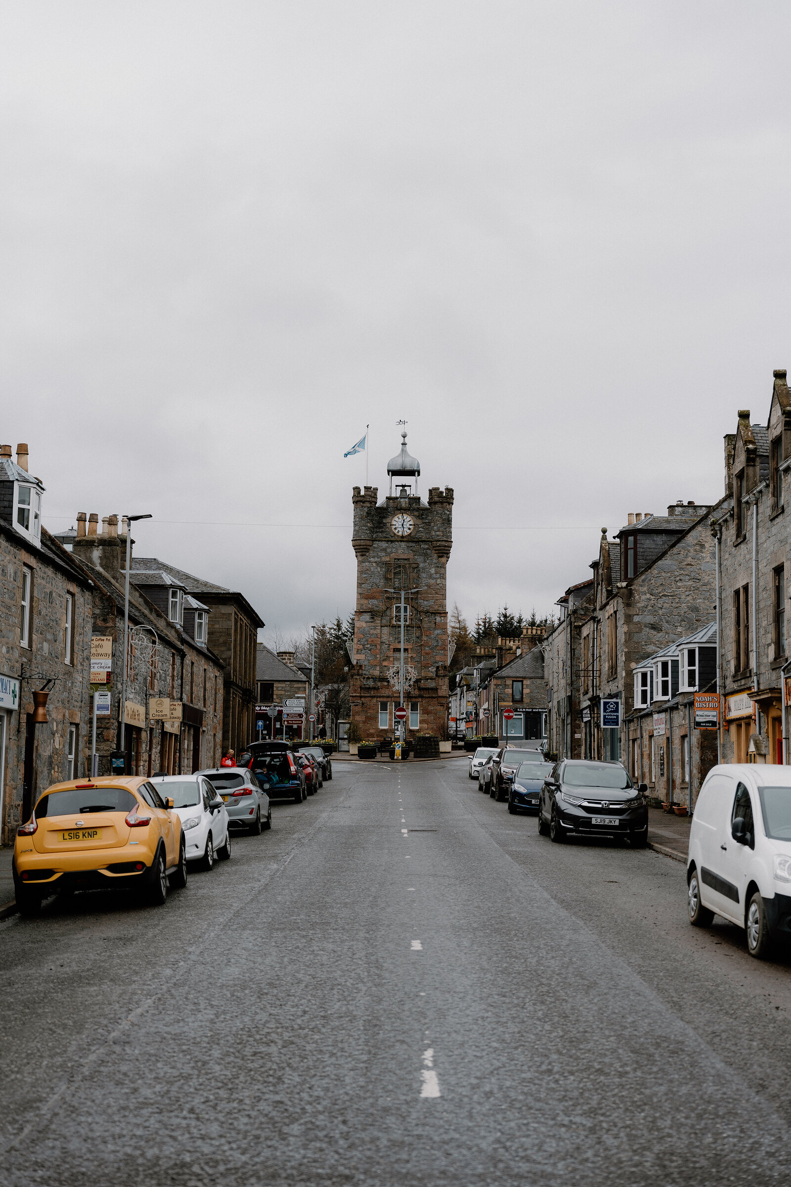 A street in Dufftown lined with granite shopfronts leads toward the town's castellated clock tower.