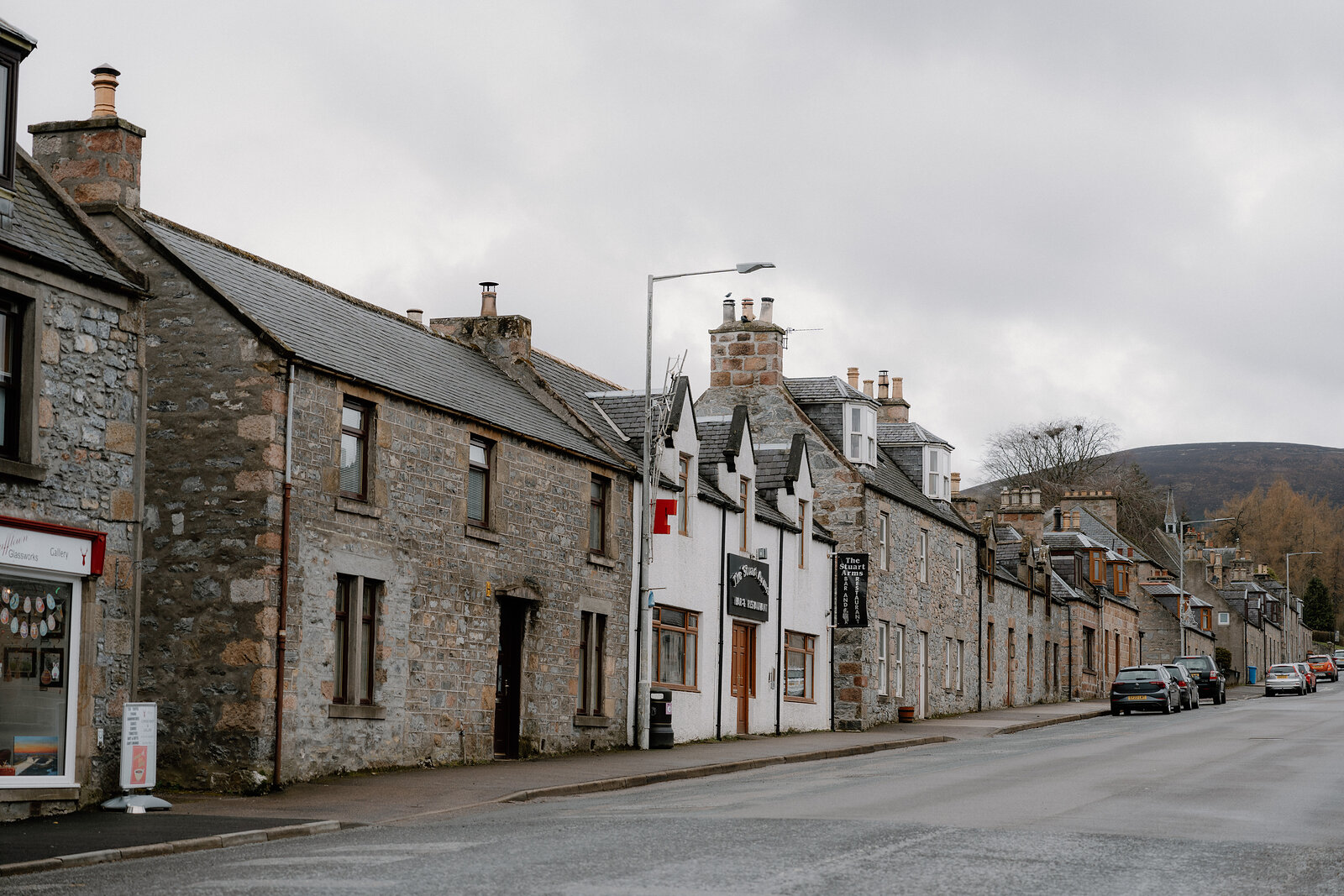 Granite buildings and a red postbox line a Dufftown street beneath a cloudy sky.