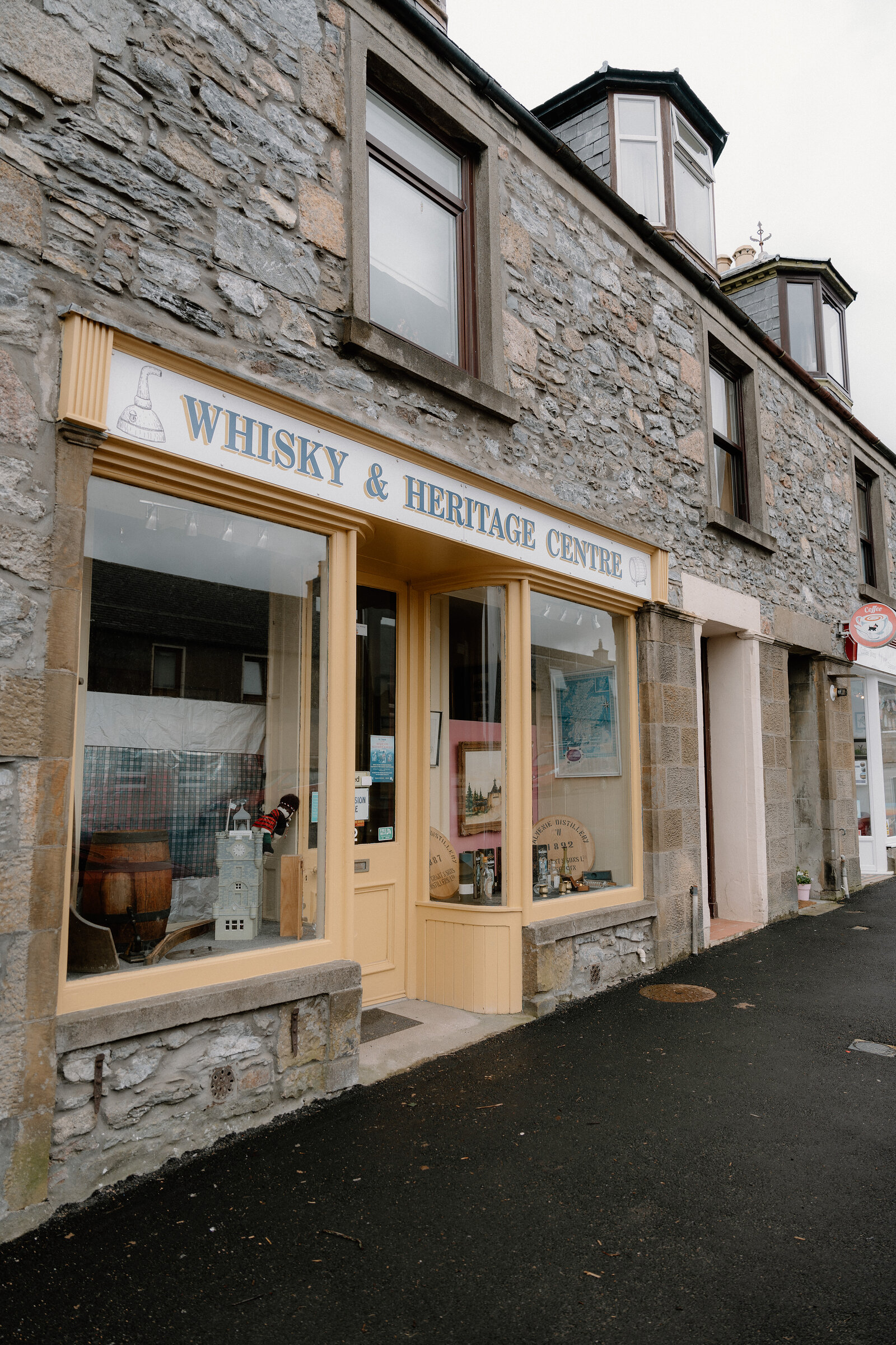 A cream shopfront lettered 'WHISKY & HERITAGE CENTRE' displays a cask and bottles in its window.
