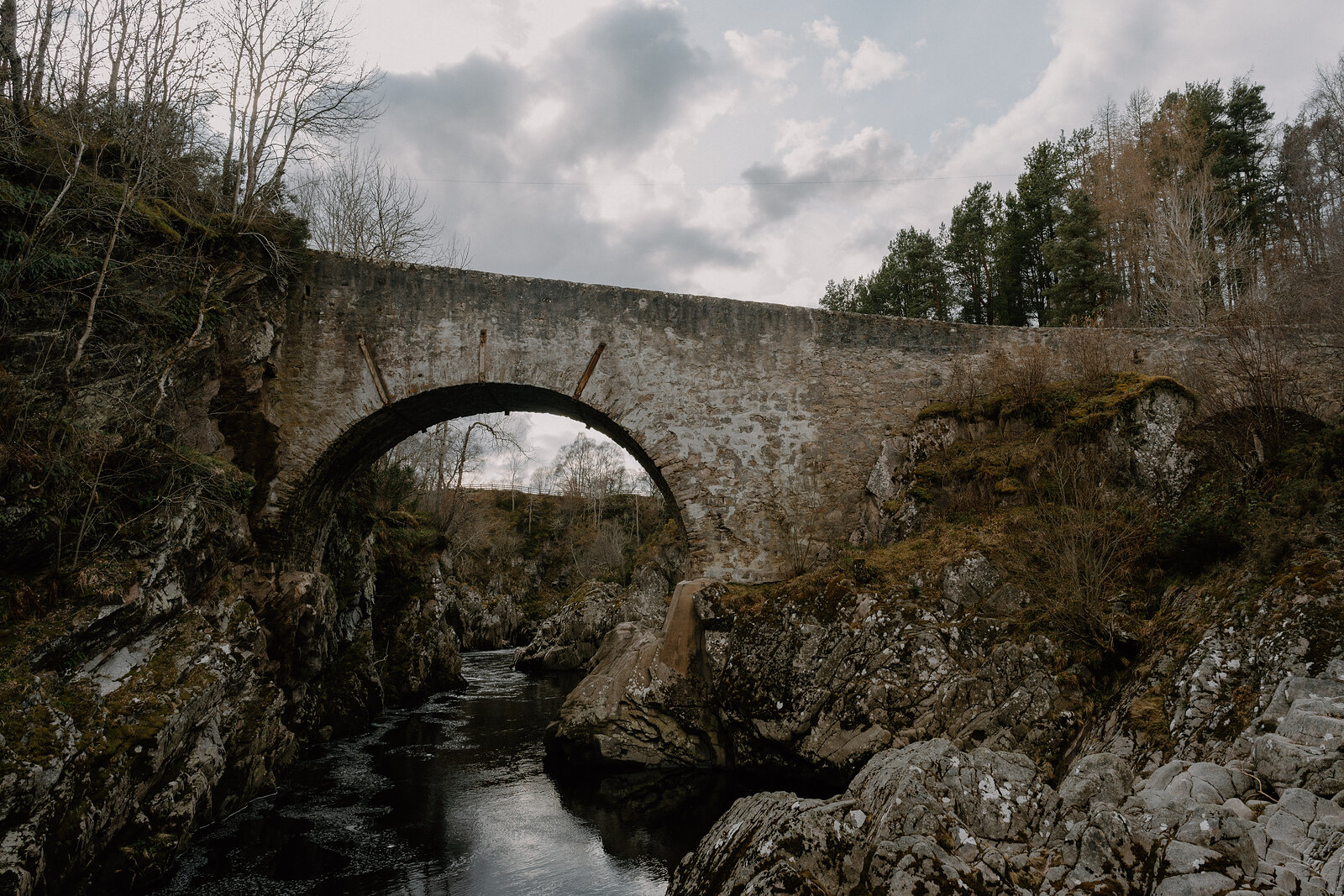 A stone arched bridge crosses a river gorge lined with autumn trees in Moray.