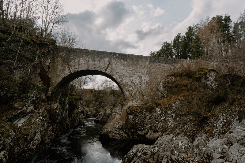 A stone arched bridge crosses a river gorge lined with autumn trees in Moray.