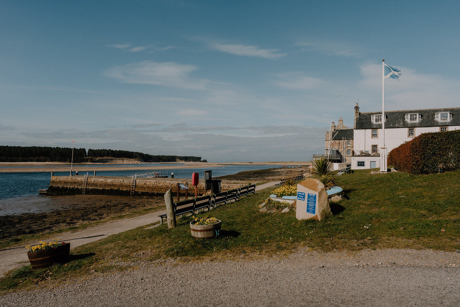 A white hotel flying the Saltire overlooks a bay along a path lined with flower planters in Moray.