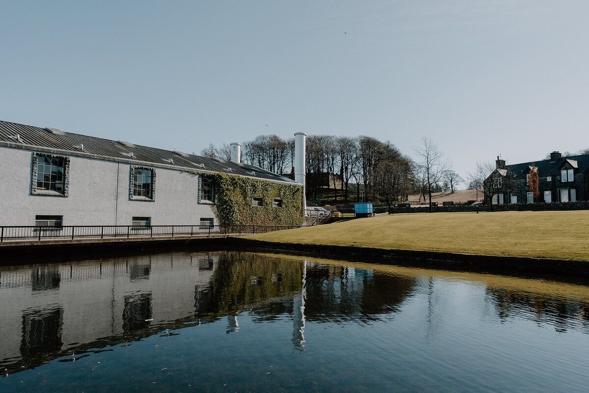 Glenfiddich Distillery's buildings and a chimney reflect in a still pond, Moray.