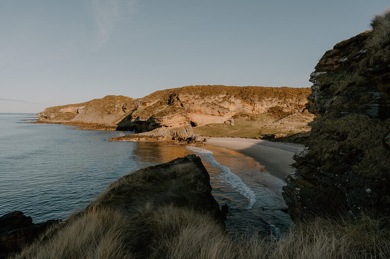 A sandy cove glows in evening light beneath rugged cliffs on the Moray coast.