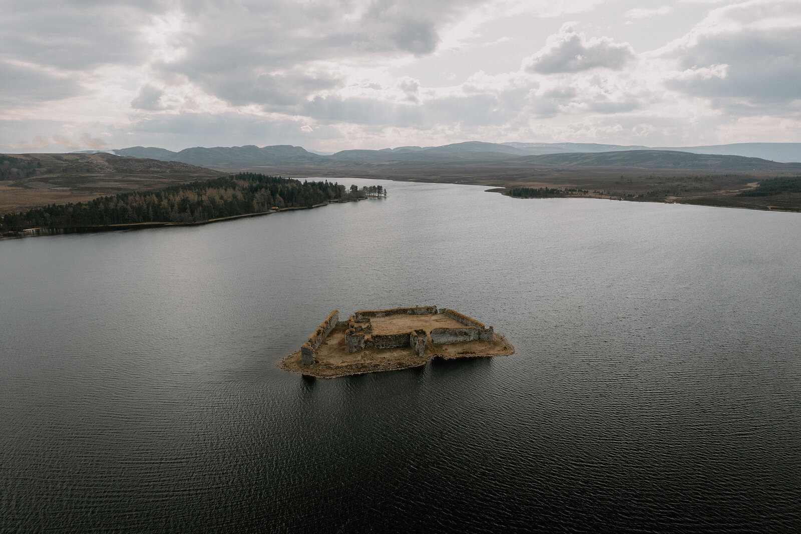 Lochindorb Castle's island ruins sit amid open water bordered by forest and hills, Moray.