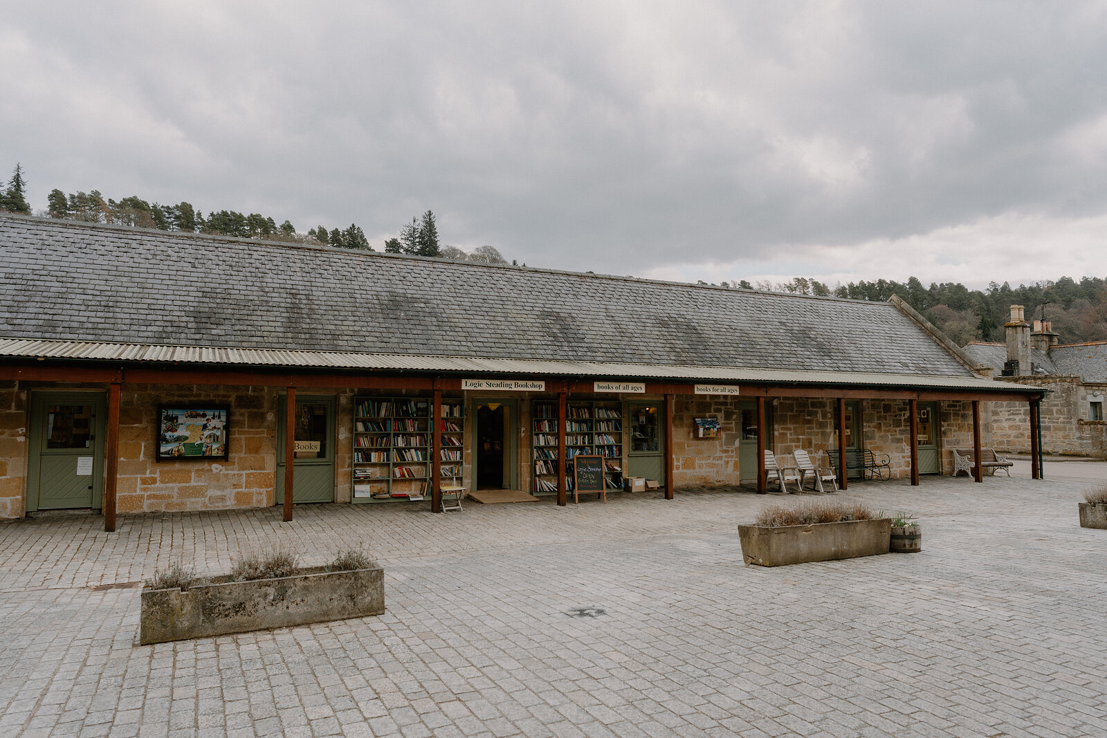 Logie Steading's shopfronts and a covered walkway line a cobbled courtyard beneath a grey sky.