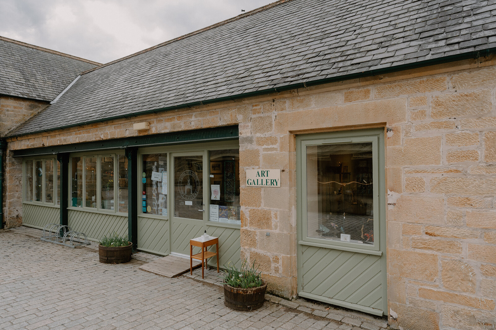 Logie Steading's Art Gallery occupies a sandstone unit with green-shuttered windows and potted plants outside.